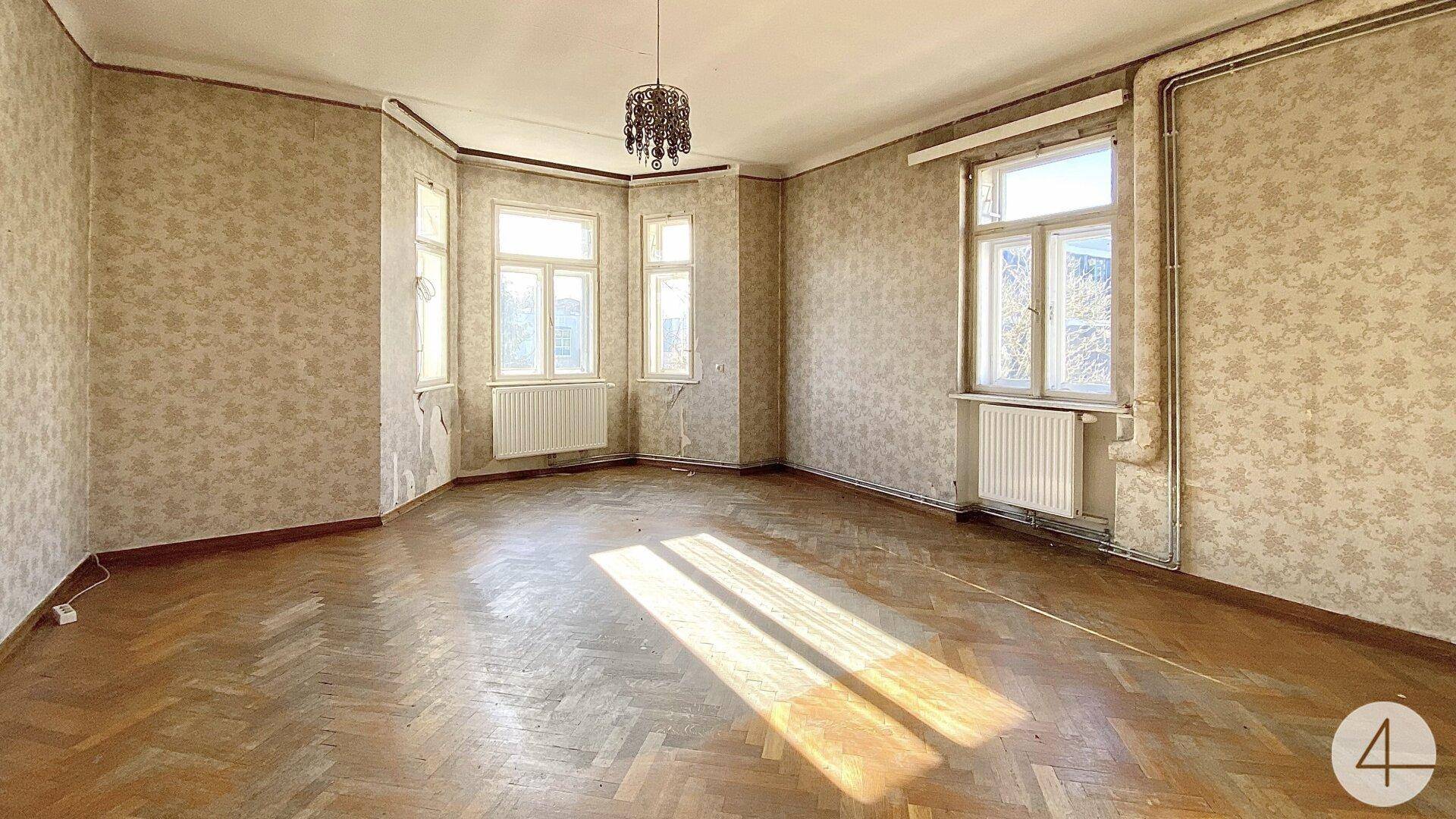 Helles Wohnzimmer mit Fischgrätparkett, gemusterter Tapete und einem Kronleuchter an der Decke.