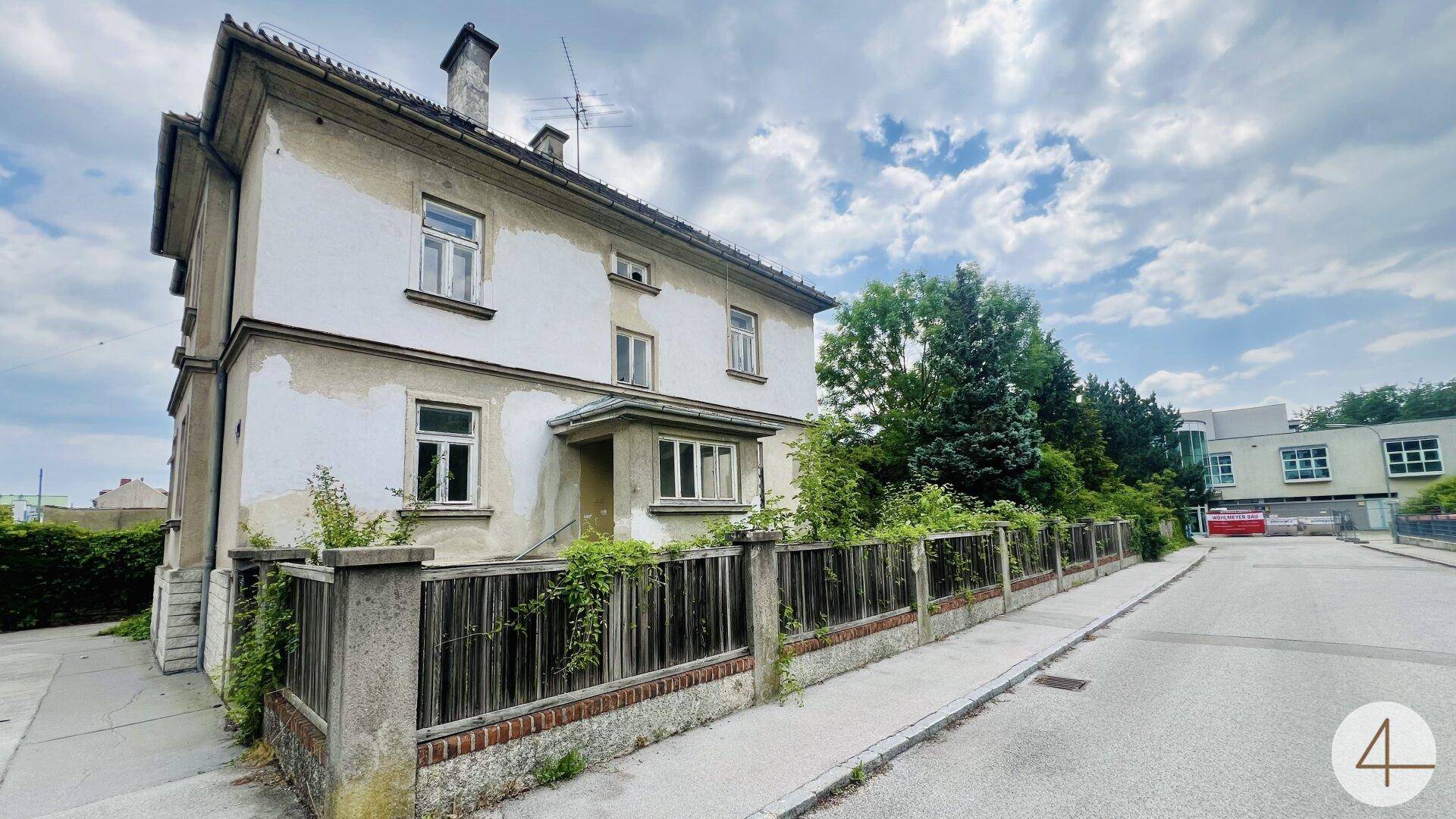 Seitenansicht des alten Gebäudes mit abblätterndem Putz und einem Zaun entlang der Straße.