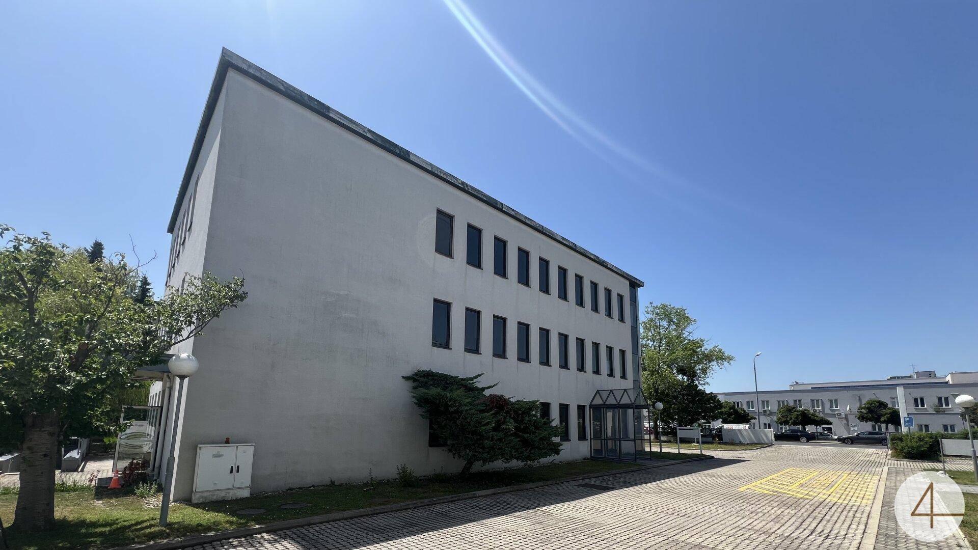 Seitenansicht eines Bürogebäudes mit vielen Fenstern und einem weitläufigen gepflasterten Bereich.
