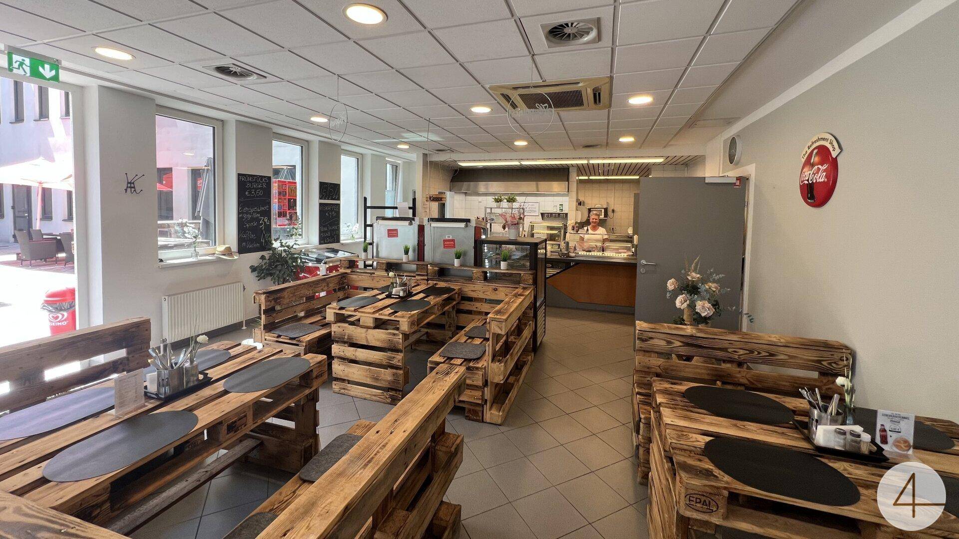 Helle Cafeteria mit rustikalen Sitzgelegenheiten aus Palettenholz und einer Ausgabetheke im Hintergrund.
