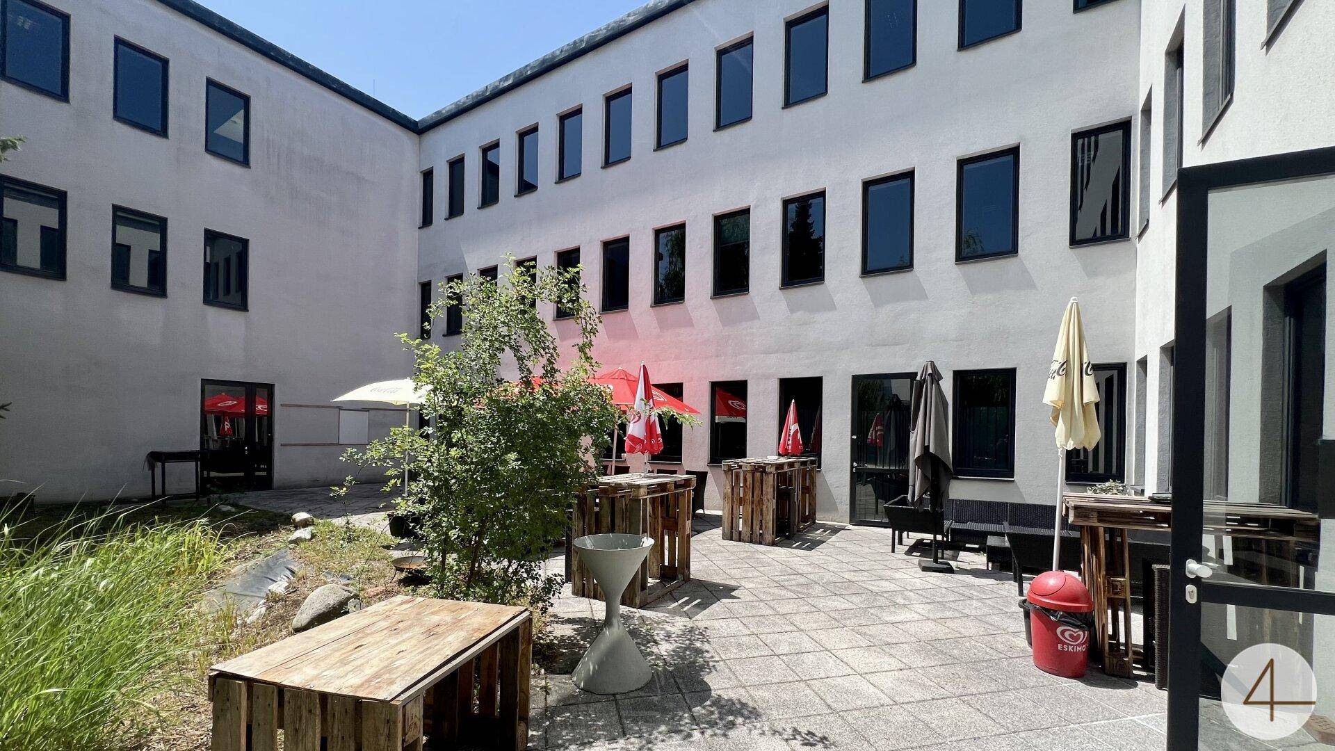 Einladender Innenhof mit Palettenmöbeln und Sonnenschirmen, ideal für Pausen im Freien.
