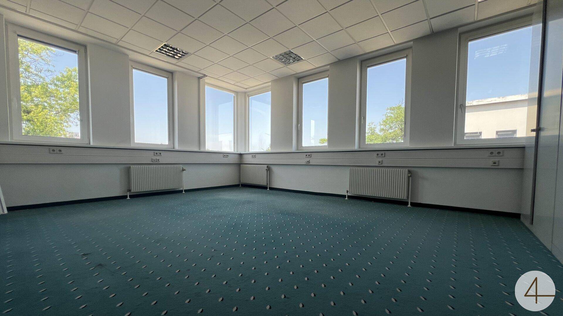 Helles Eckbüro mit Teppichboden und großen Fenstern, die eine angenehme Arbeitsatmosphäre schaffen.