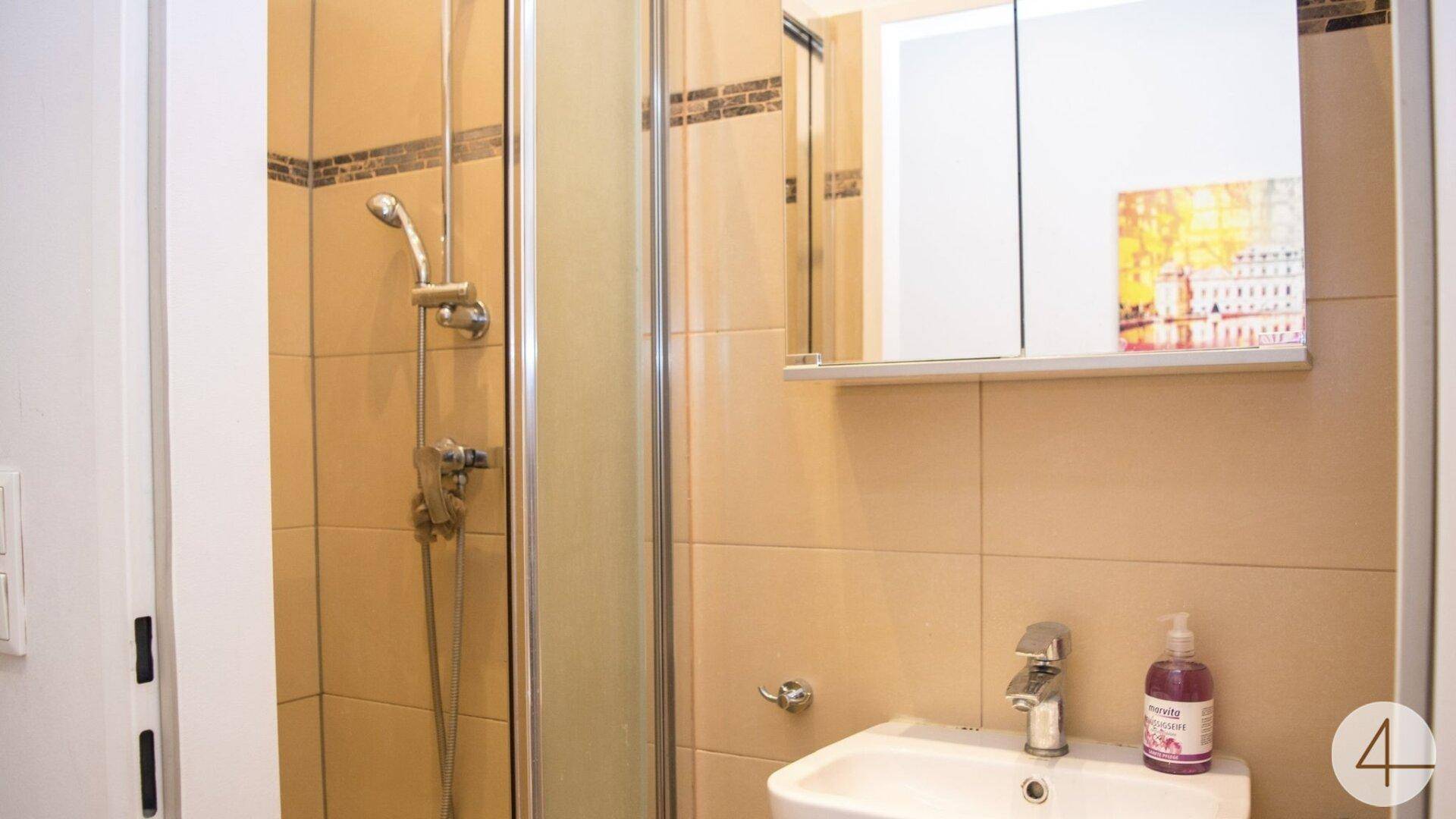 Badezimmer mit Duschkabine, beigefarbenen Fliesen und Spiegelschrank über dem Waschbecken.