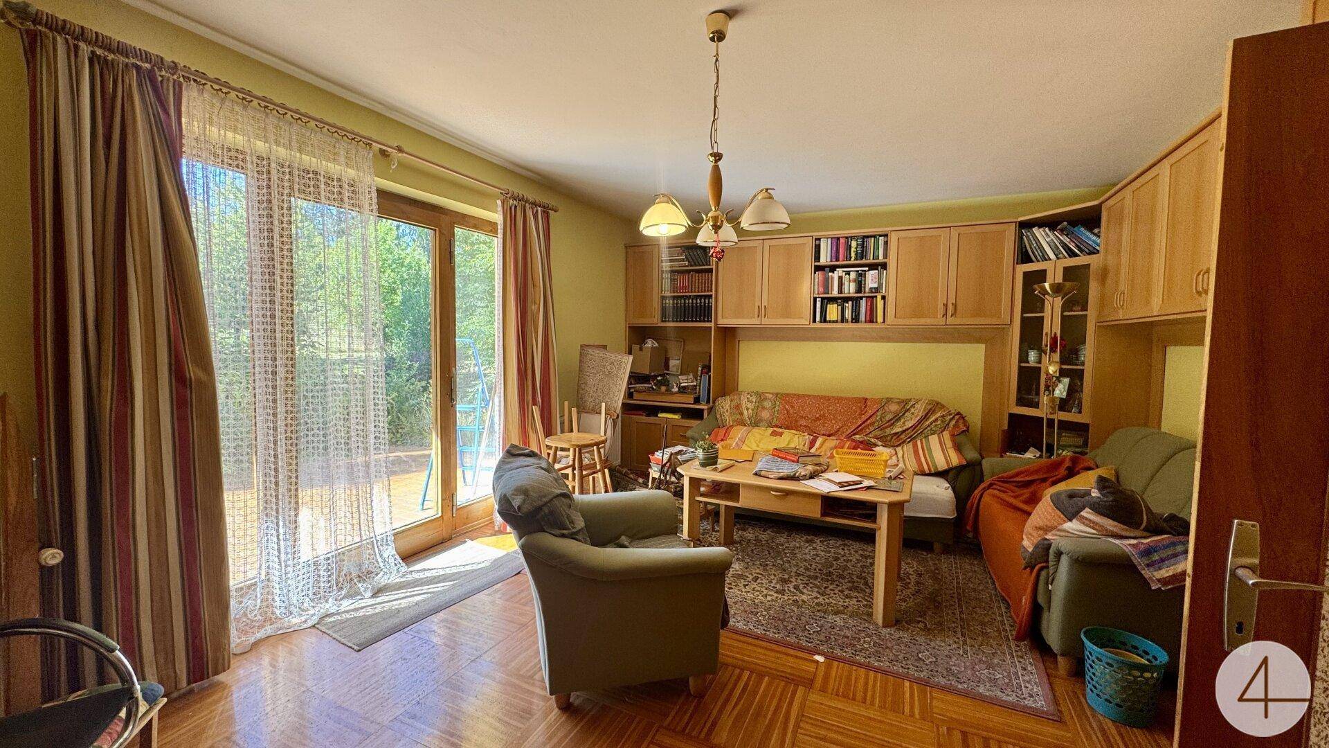 Helles Wohnzimmer mit Holzmöbeln, bequemen Sitzgelegenheiten und Zugang zum Außenbereich.