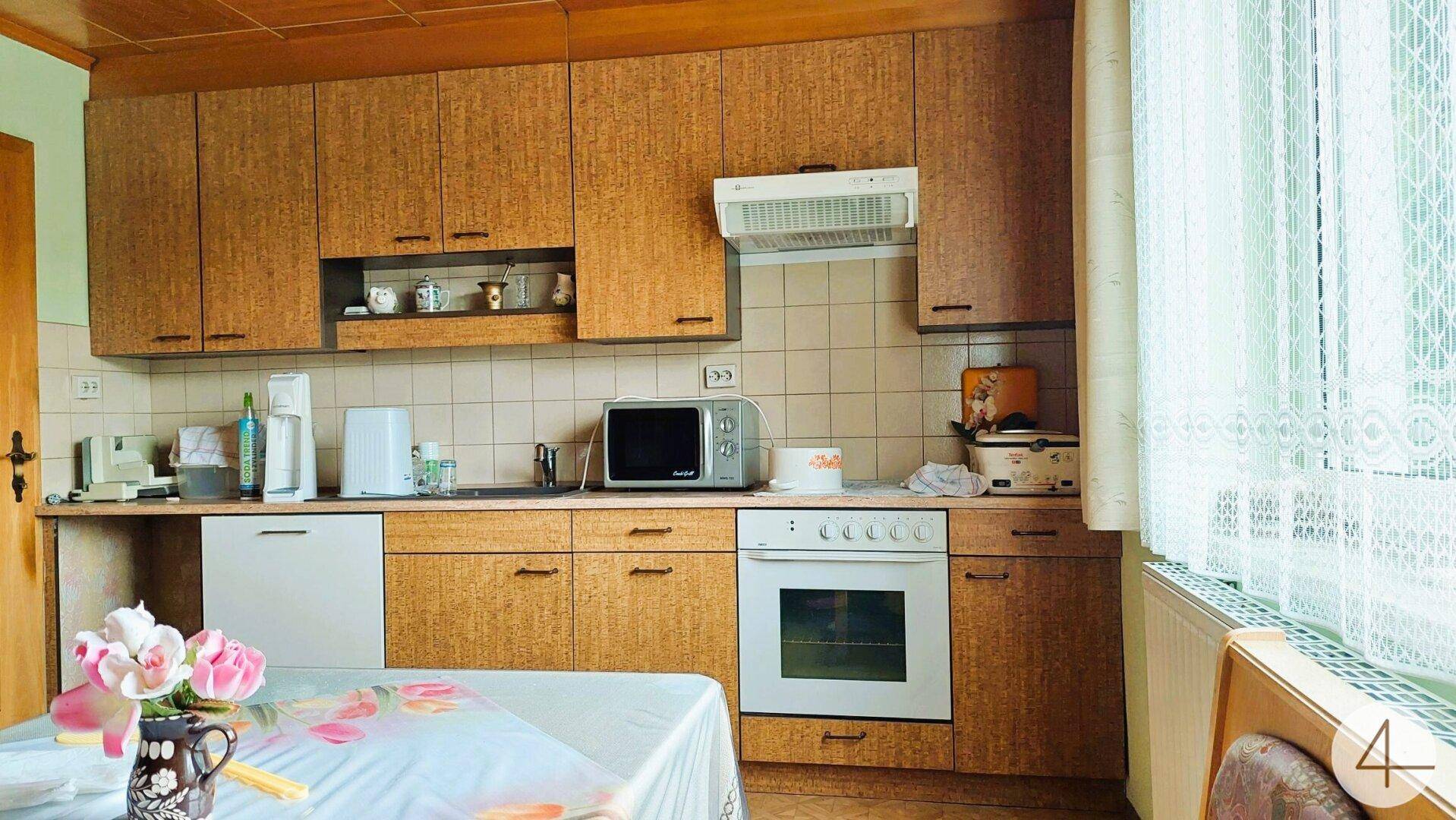 Funktionale Küche mit älteren Holzschränken, Fliesenrückwand und grundlegenden Geräten.