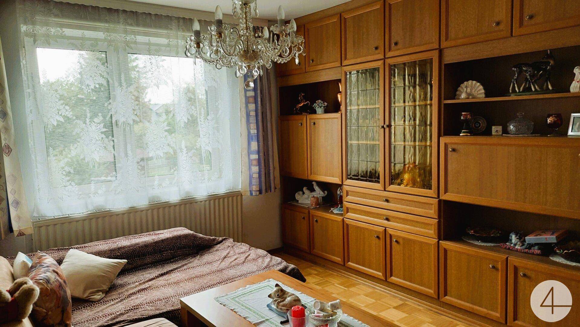 Wohnzimmer mit Holzschrankwand, Parkettboden und Kronleuchter, Blick ins Grüne.