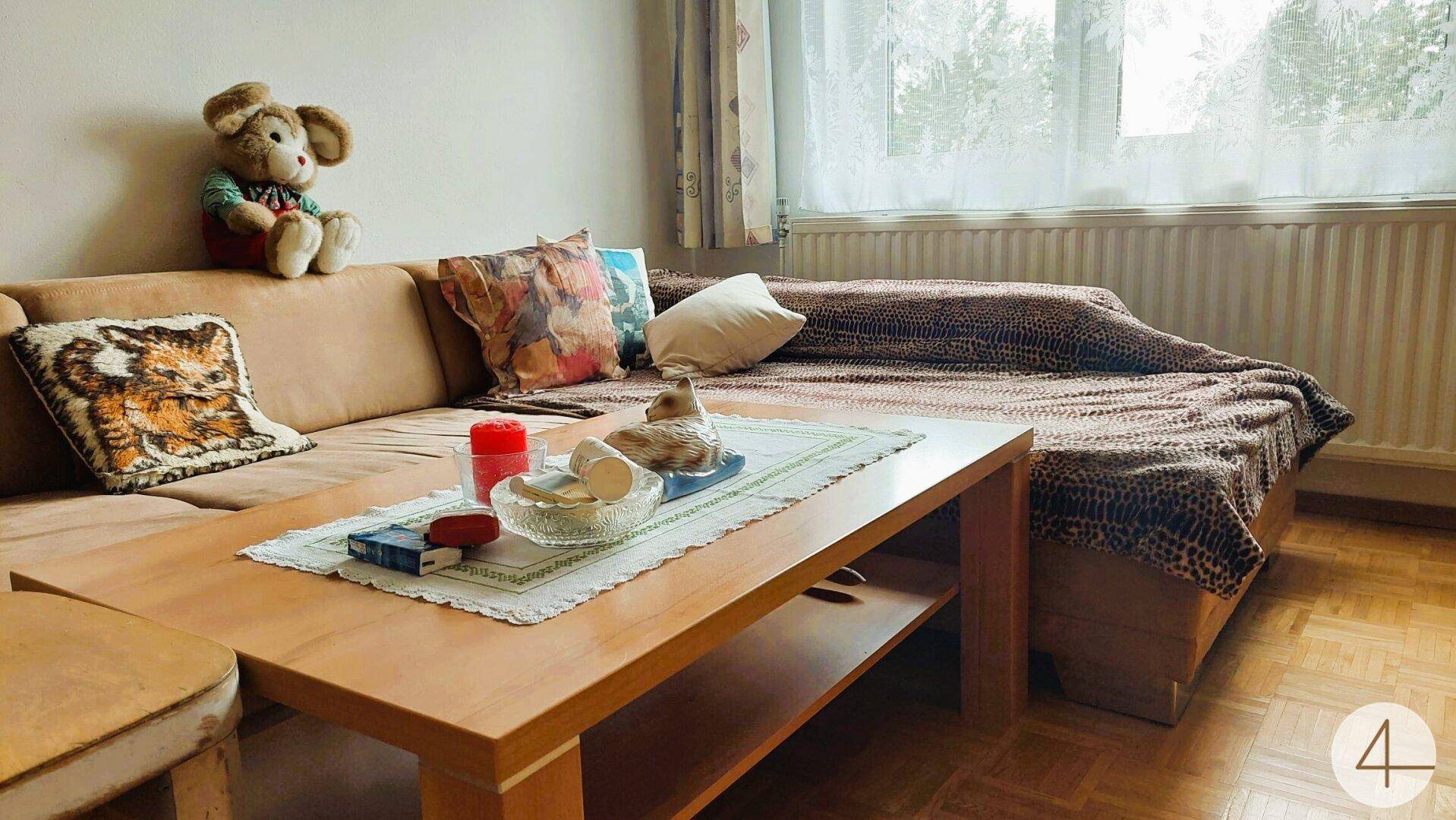 Gemütliches Wohnzimmer mit Sofa, Couchtisch und Blick durch das Fenster ins Freie.