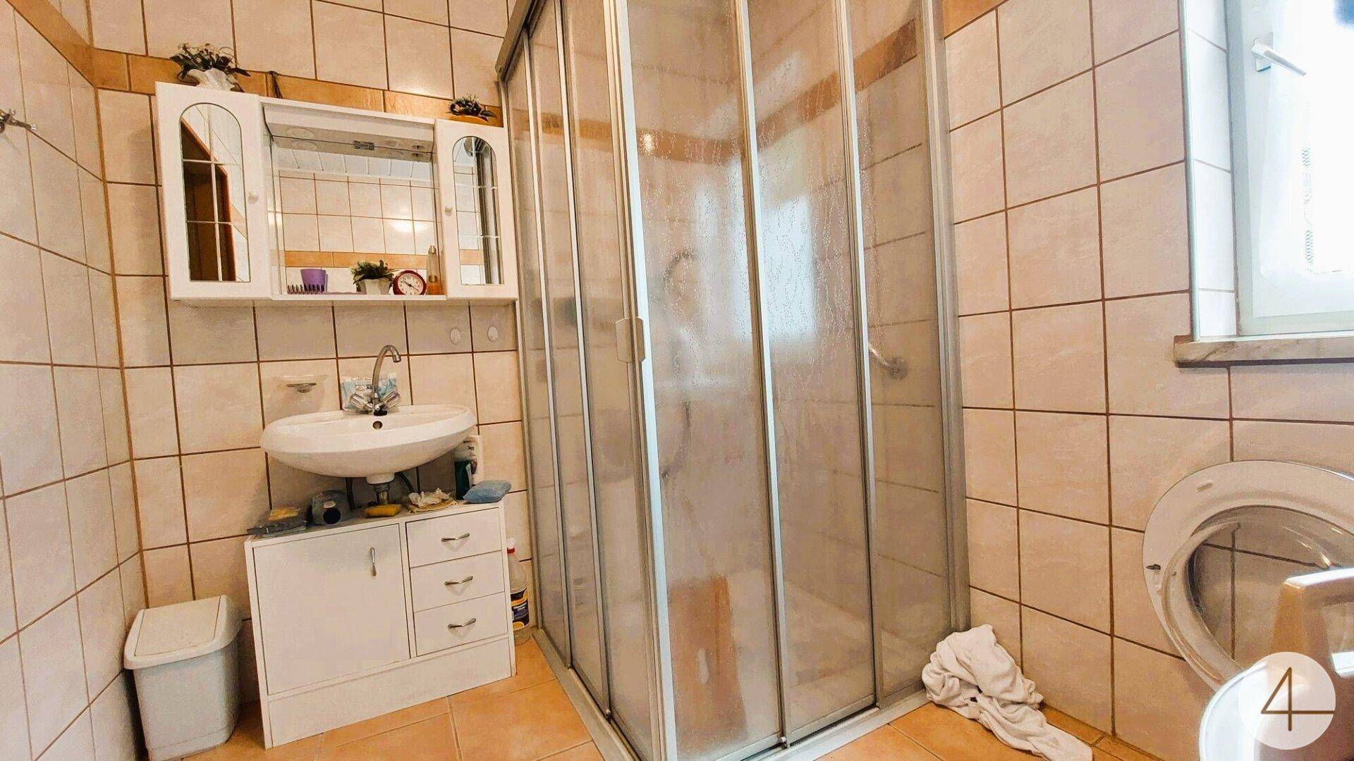 Badezimmer mit Duschkabine, Waschbecken und hellen Fliesen in Beige- und Brauntönen.