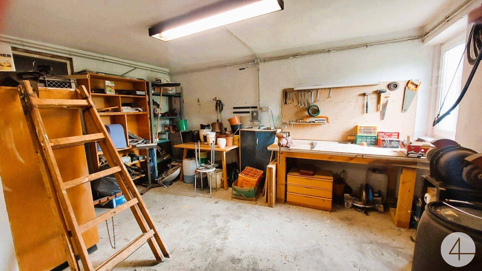 Geräumige Werkstatt mit Regalen, Werkbank und verschiedenen Arbeitsmaterialien.