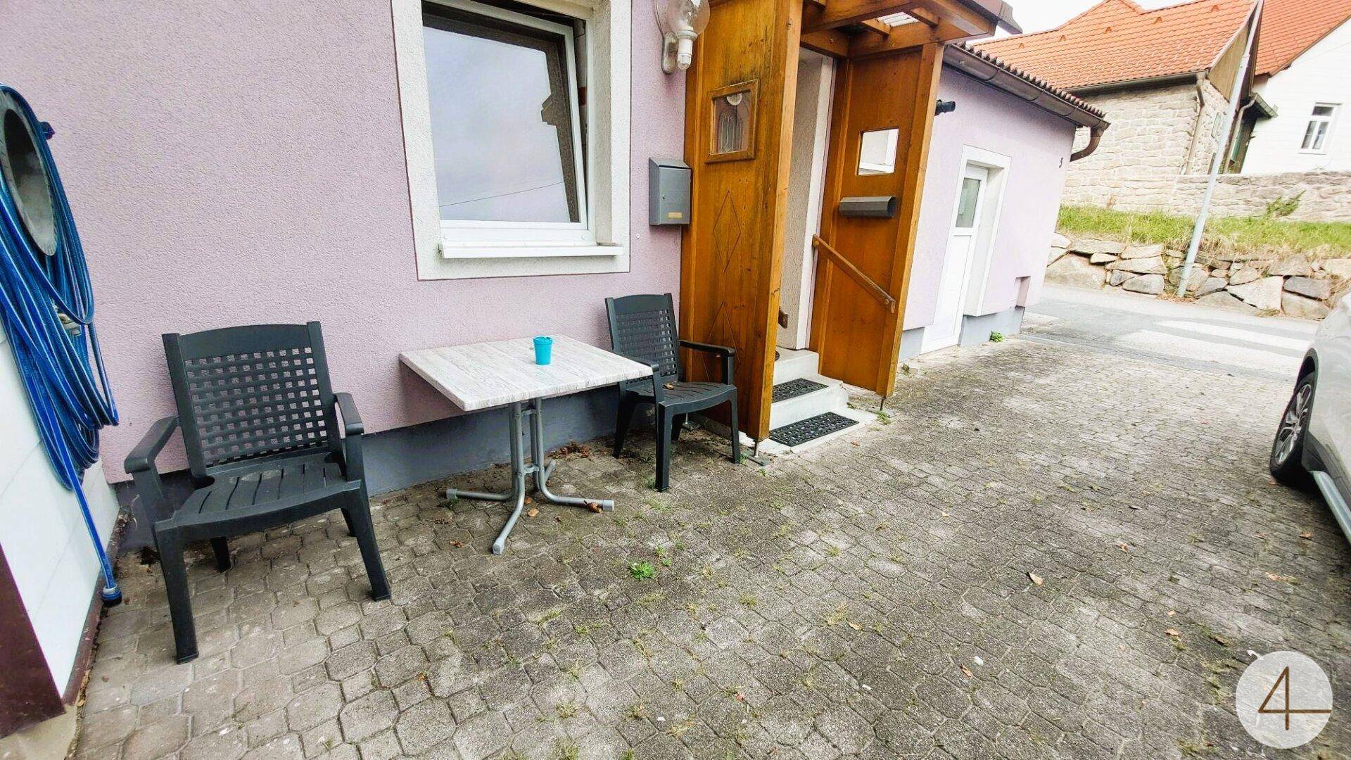 Kleiner gepflasterter Außenbereich mit Tisch und Stühlen vor dem Hauseingang.