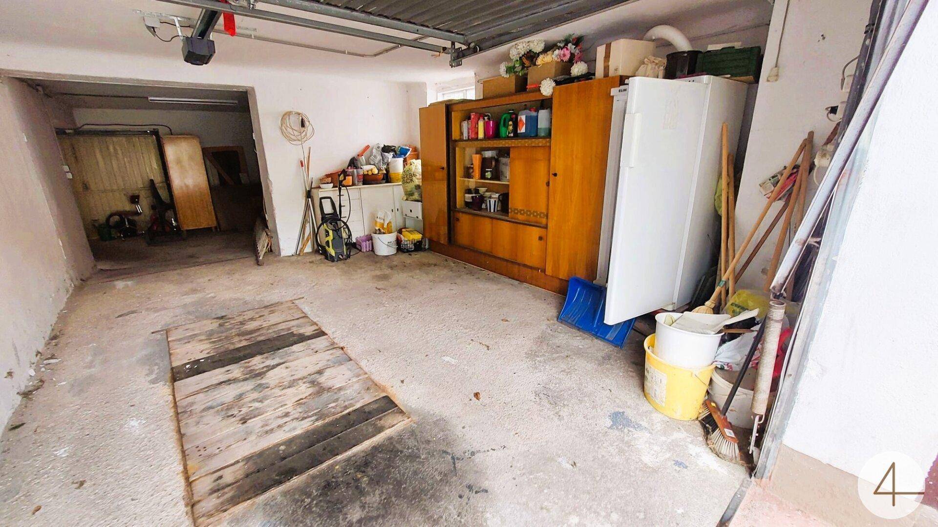 Garage mit Betonboden, Lagerflächen und einem großen Tor.