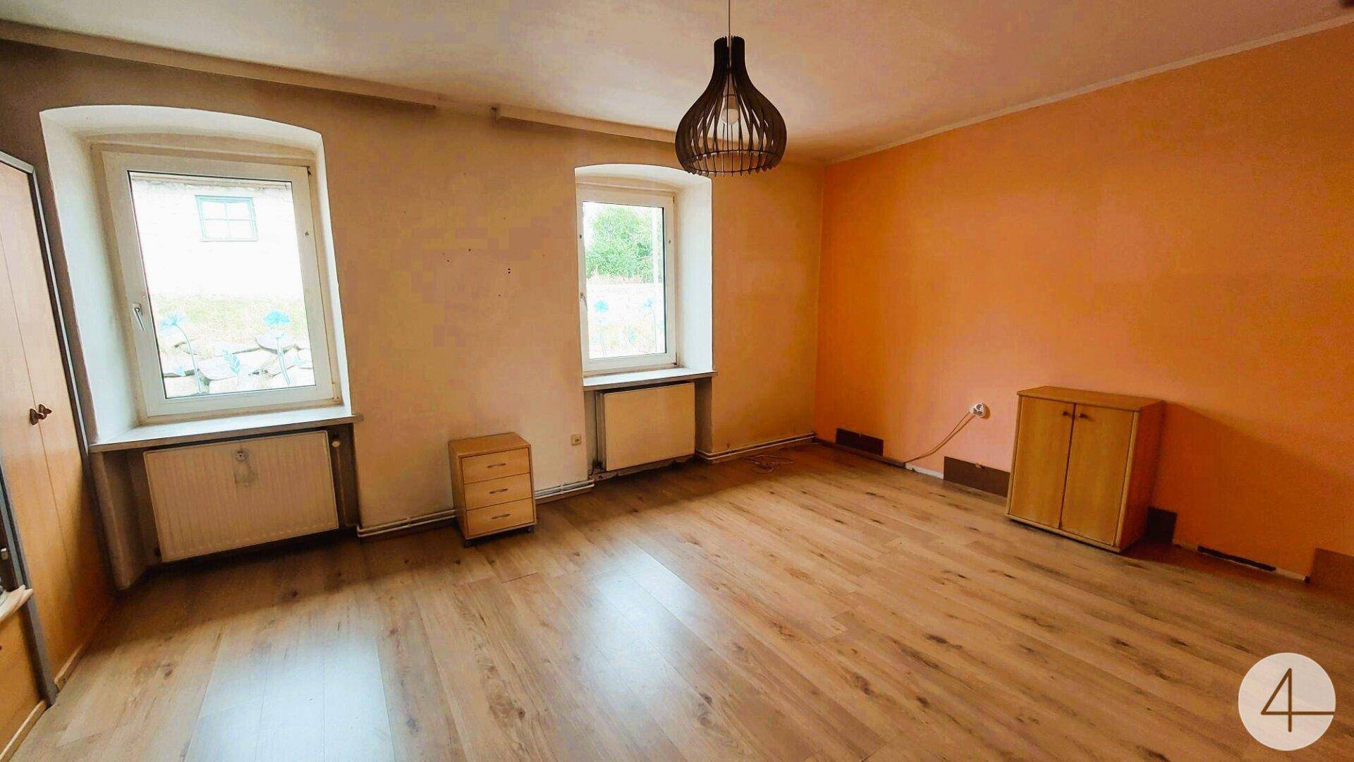 Geräumiges Zimmer mit zwei Fenstern, Laminatboden und einfacher Wandgestaltung in Orange.