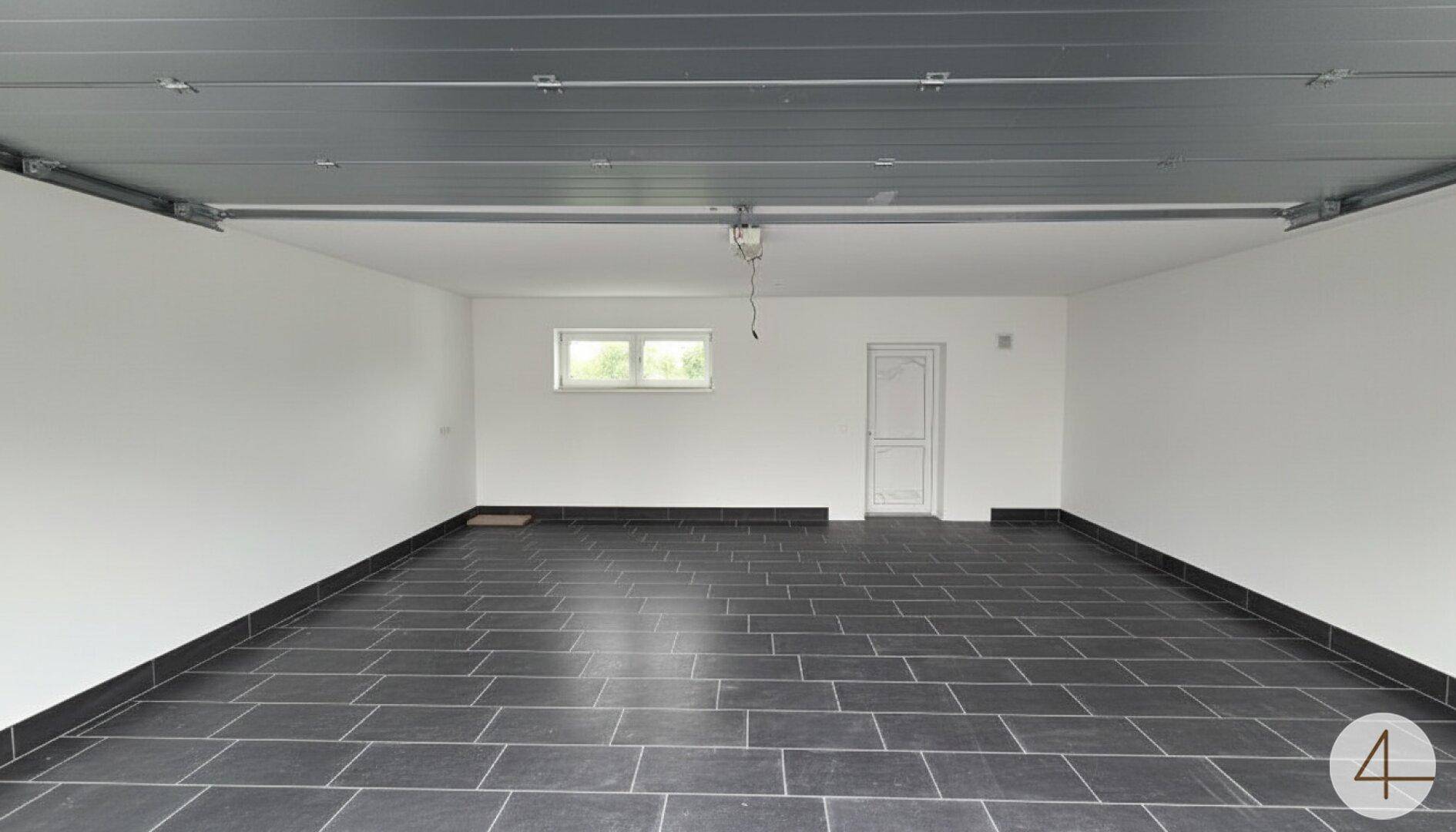 Geräumige Garage im Neubau mit dunklen Fliesen und einem Fenster, bereit zur Nutzung.