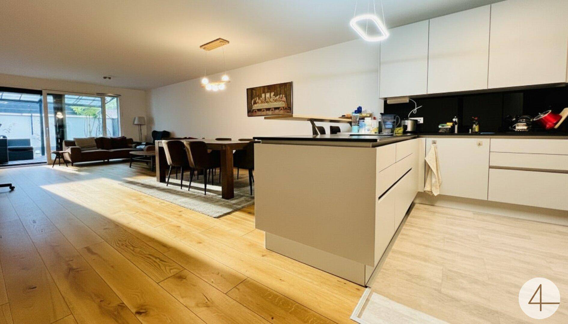 Offener Wohn- und Essbereich mit moderner Küche, Holzboden und Zugang zur Terrasse.