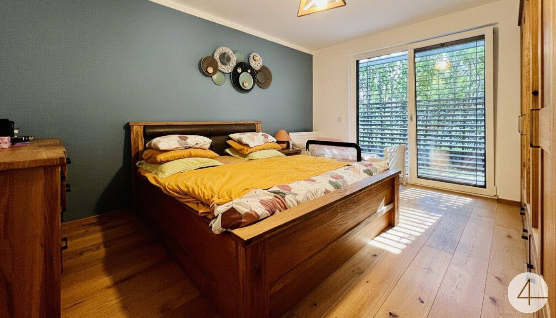 Gemütliches Schlafzimmer mit Holzbett, blauer Akzentwand und viel Tageslicht.