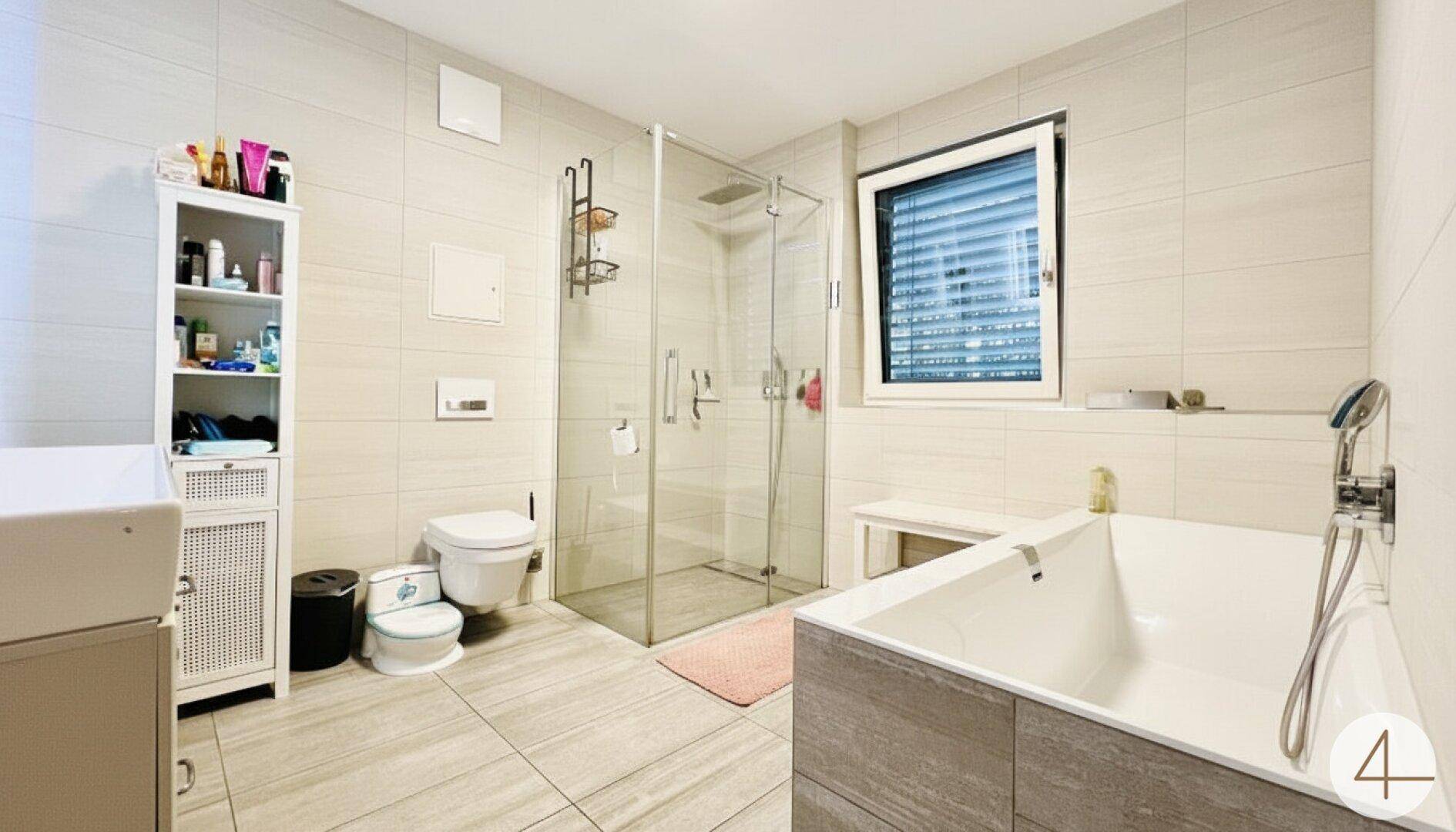 Modernes Badezimmer mit Badewanne, ebenerdiger Dusche, Fenster und hellen Fliesen.