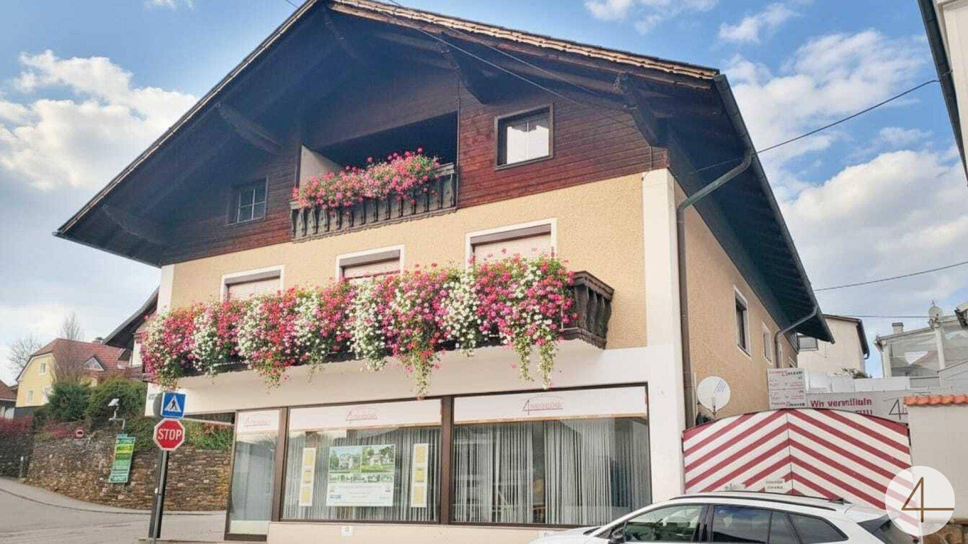 Traditionelles Gebäude mit blumengeschmückten Balkonen und einem Geschäft im Erdgeschoss.