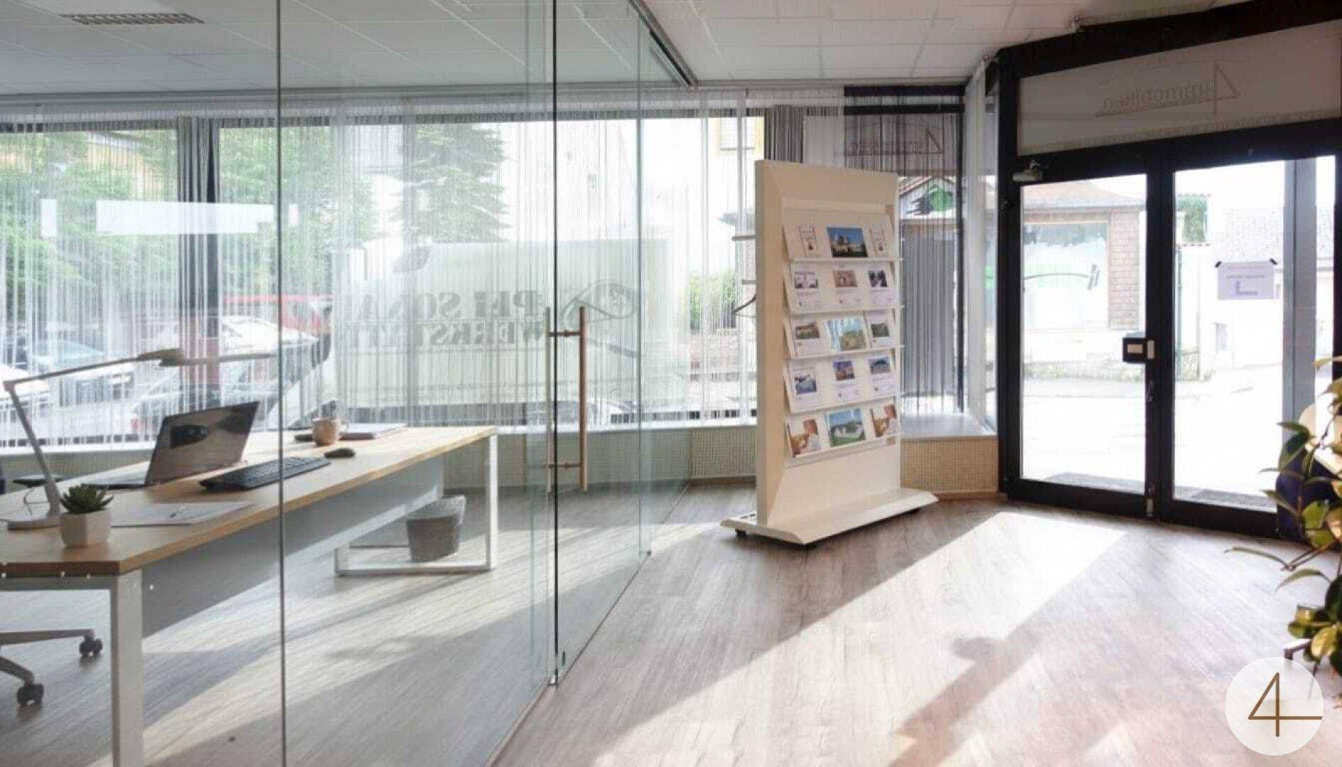 Modernes Büro mit Glaswänden, Holzboden und viel Tageslicht.