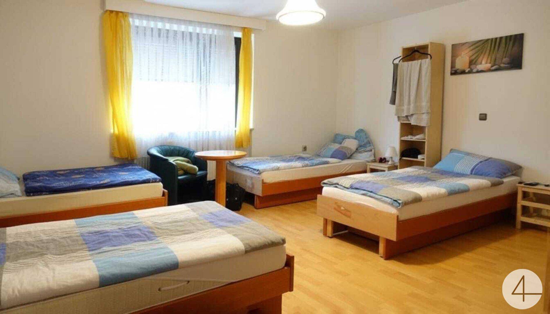 Helles Schlafzimmer mit mehreren Einzelbetten, Holzfußboden und gelben Vorhängen.