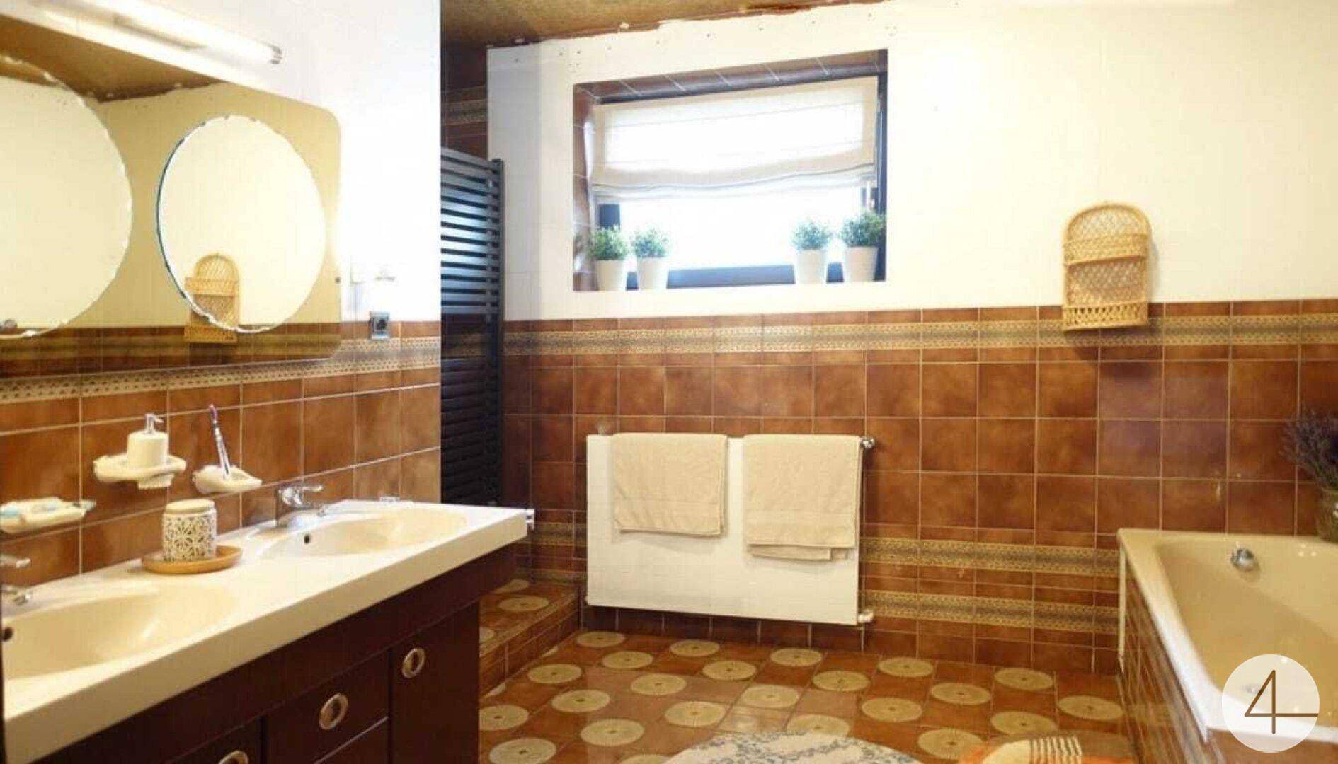 Badezimmer im 80er-Jahre-Stil mit braunen Fliesen, Doppelwaschbecken und Badewanne.