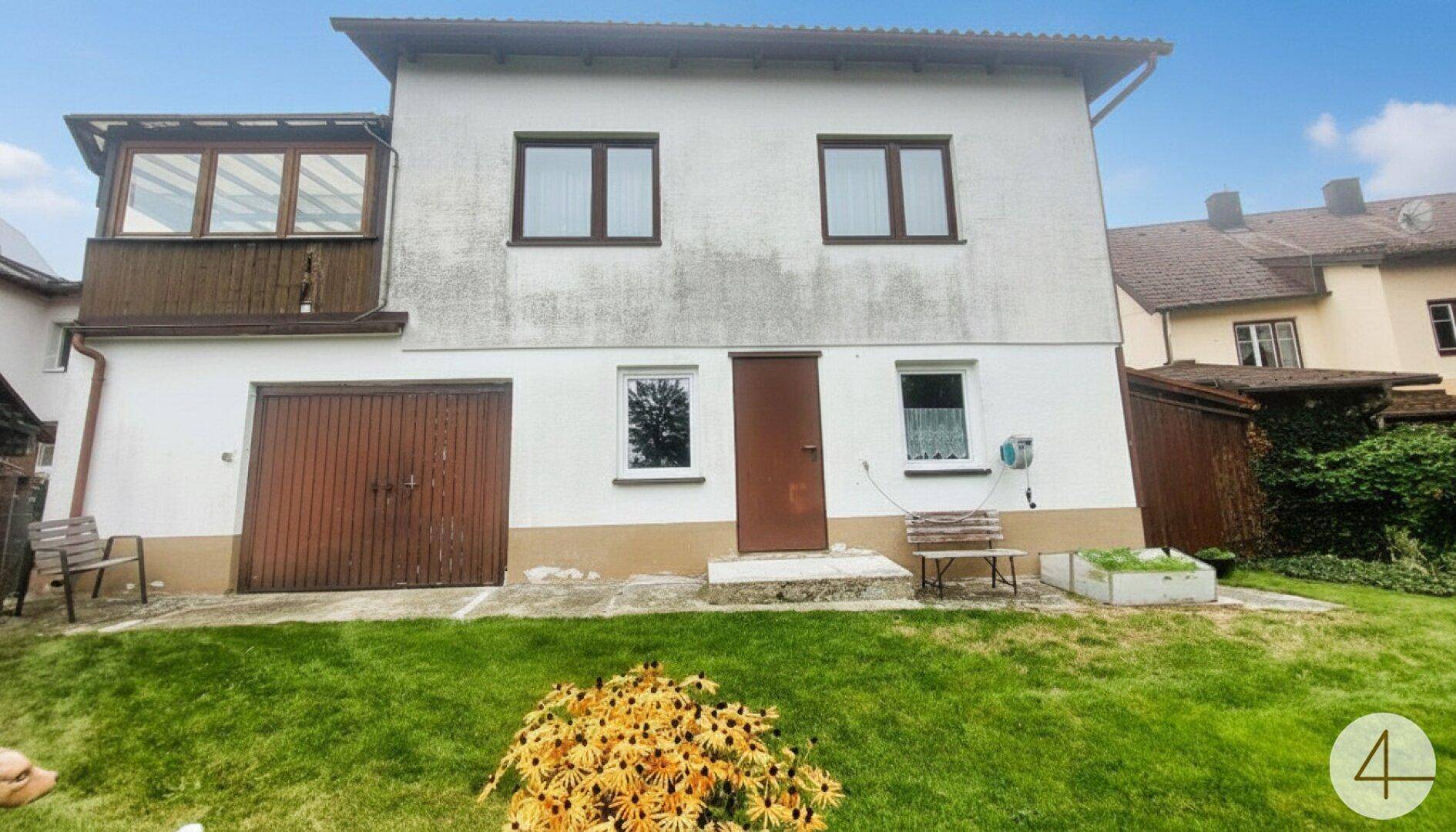 Rückseite des Hauses mit Garage, kleinem Gartenbereich und einem Balkon im Obergeschoss.