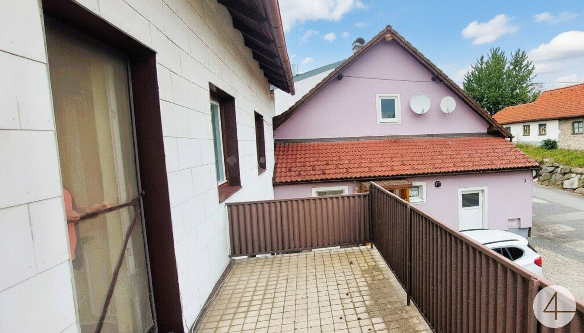 Kleiner Balkon mit Fliesenboden und braunem Geländer, bietet einen Blick auf die Nachbarhäuser.