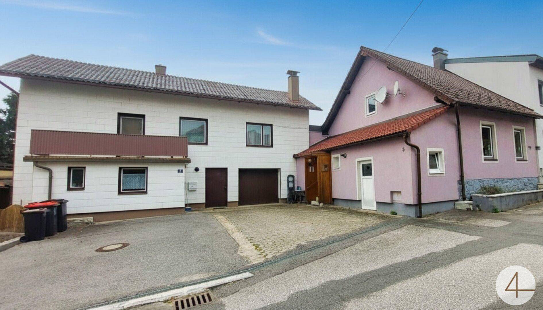 Ansicht von zwei Wohnhäusern mit gemeinsamer Zufahrt und Garagenzugang unter blauem Himmel.