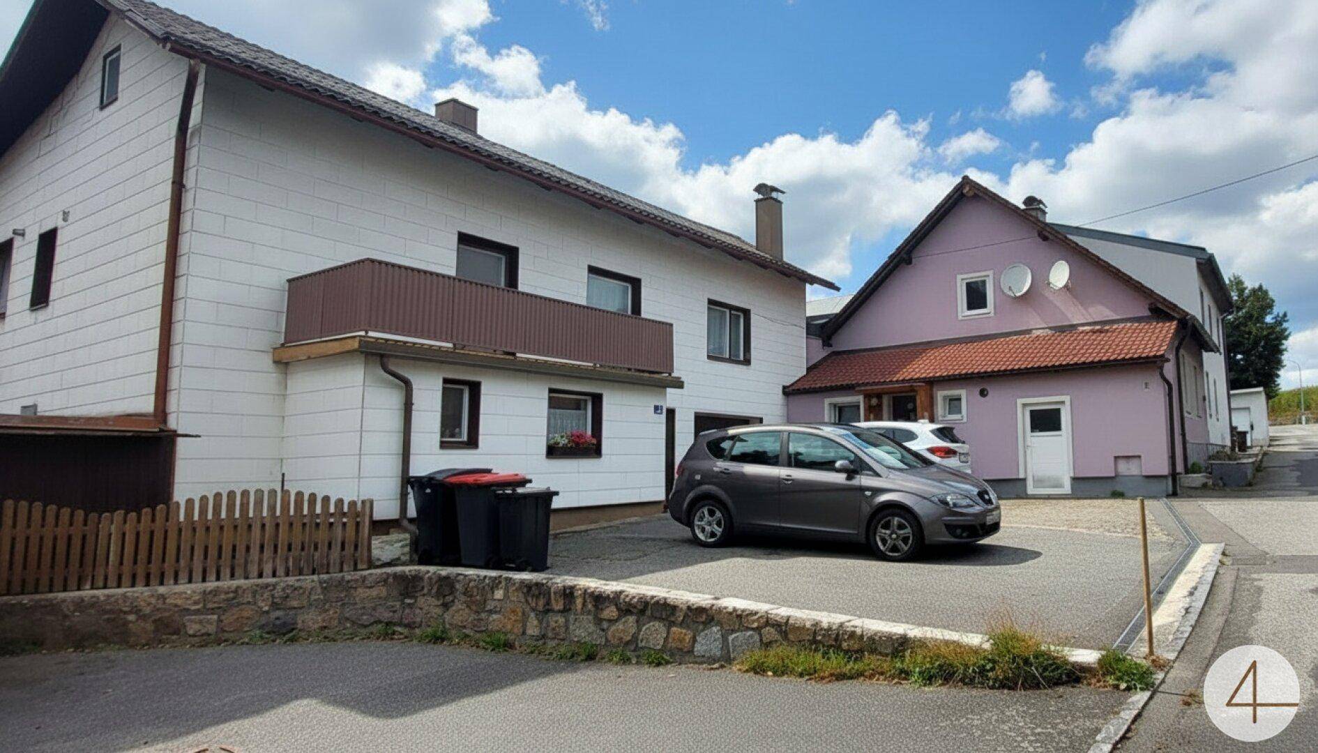 Blick auf die beiden Wohnhäuser von der Straße mit einem geparkten Auto auf dem gemeinsamen Hof.