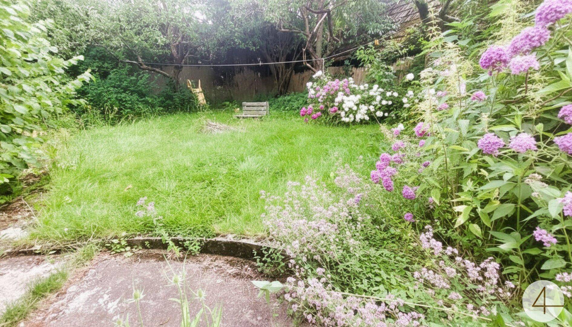 Blühender Garten mit farbenfrohen Blumenbeeten, Rasenfläche und altem Baumbestand.