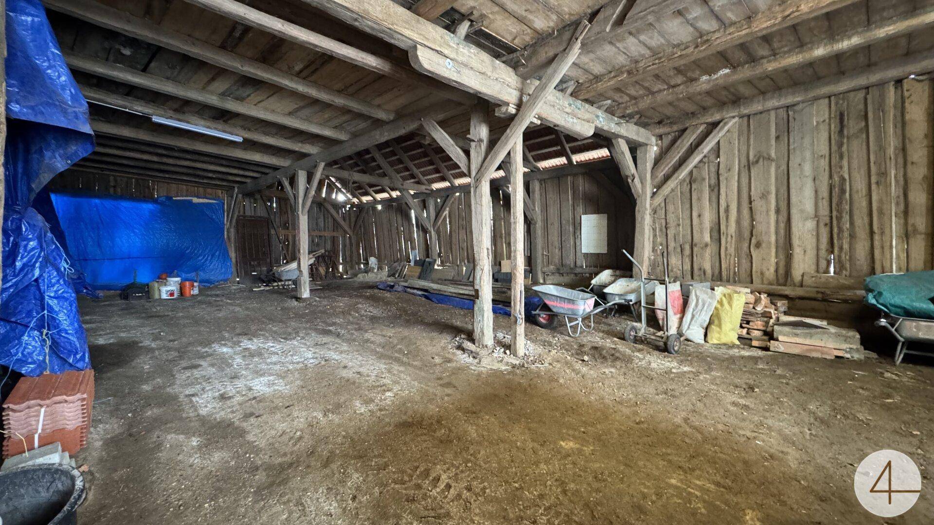 Geräumiger, rustikaler Scheuneninnenraum mit Holzbalken und Erdboden, genutzt als Lagerfläche.