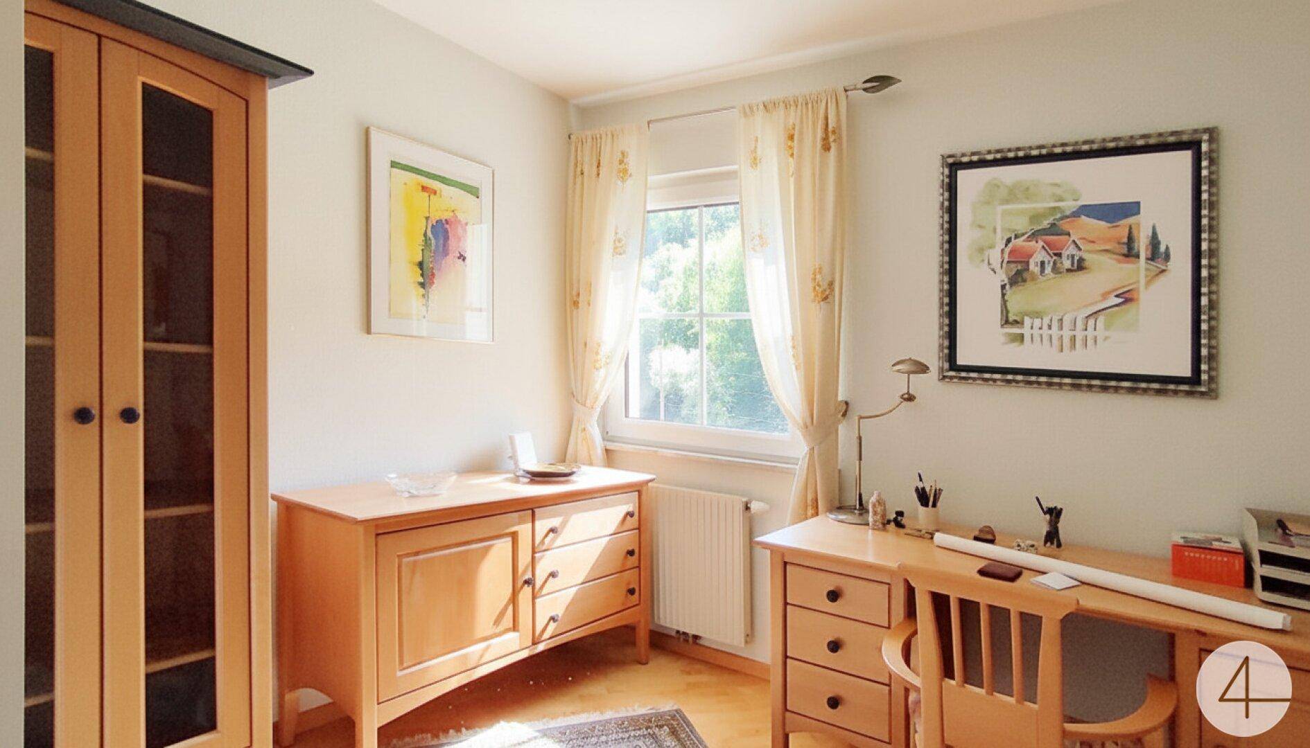 Helles Arbeitszimmer mit Holzmöbeln, großem Fenster und Blick ins Grüne.