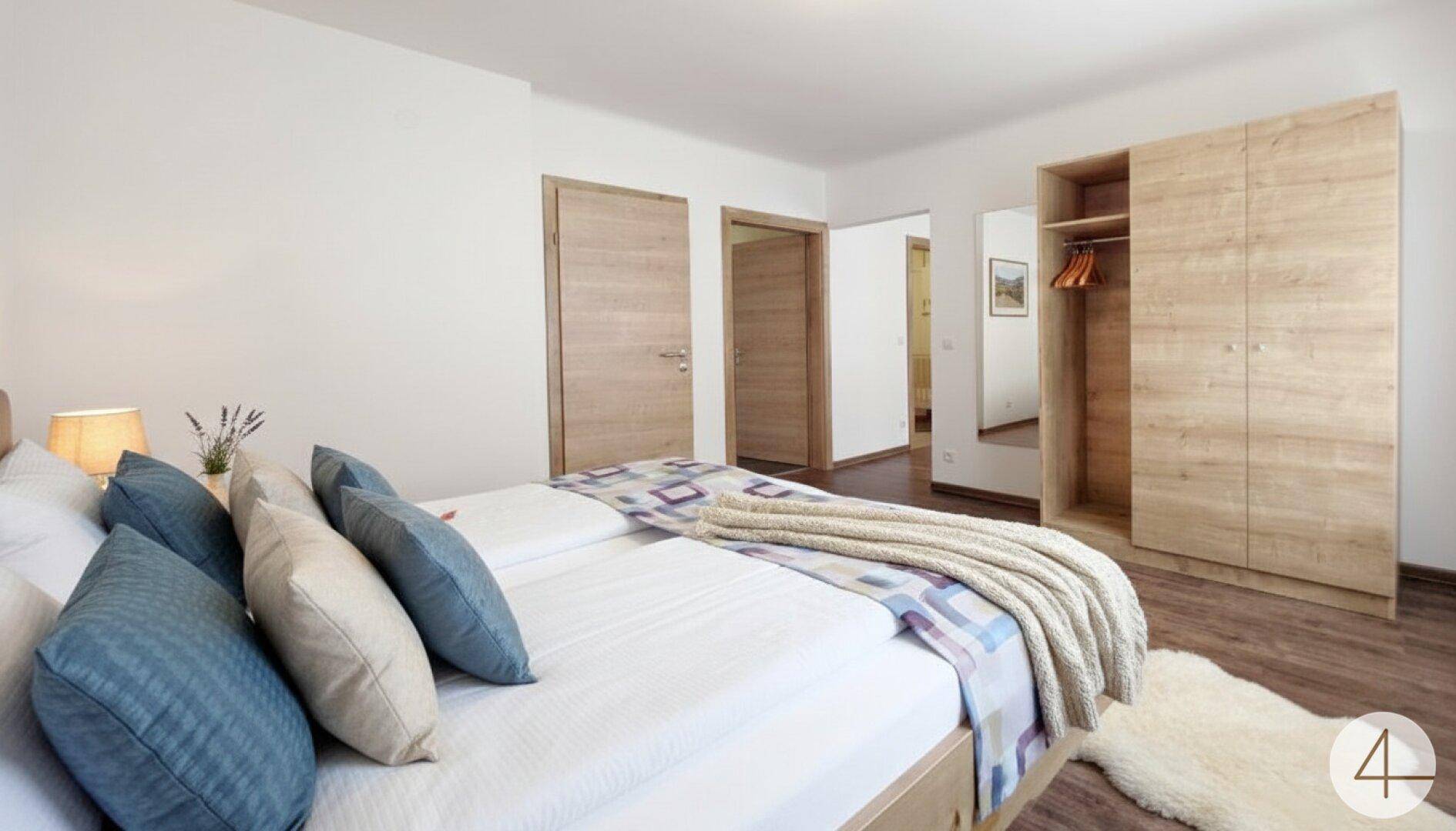 Helles Schlafzimmer mit Doppelbett, Holzschrank und Blick in den Flur.
