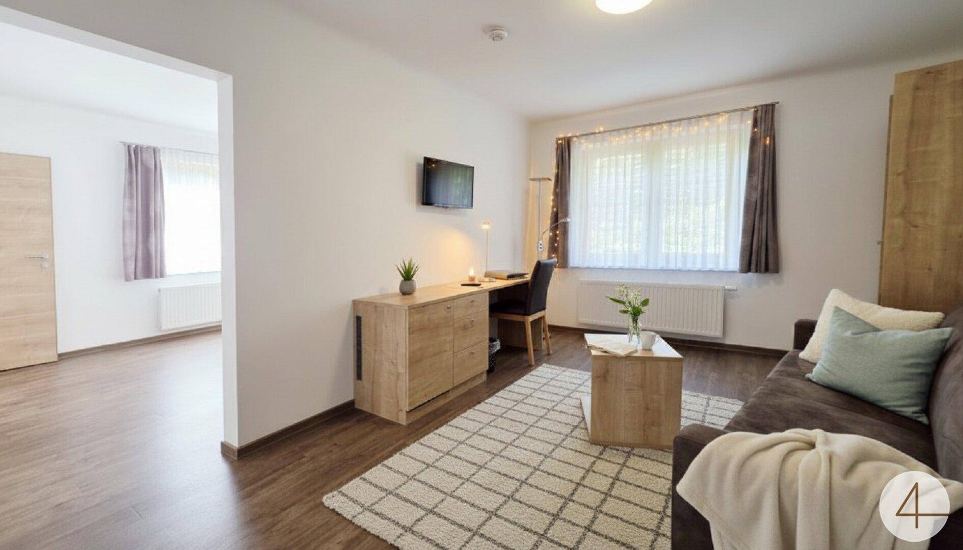 Heller Wohnbereich mit Sofa, Schreibtisch und Blick in einen angrenzenden Raum.