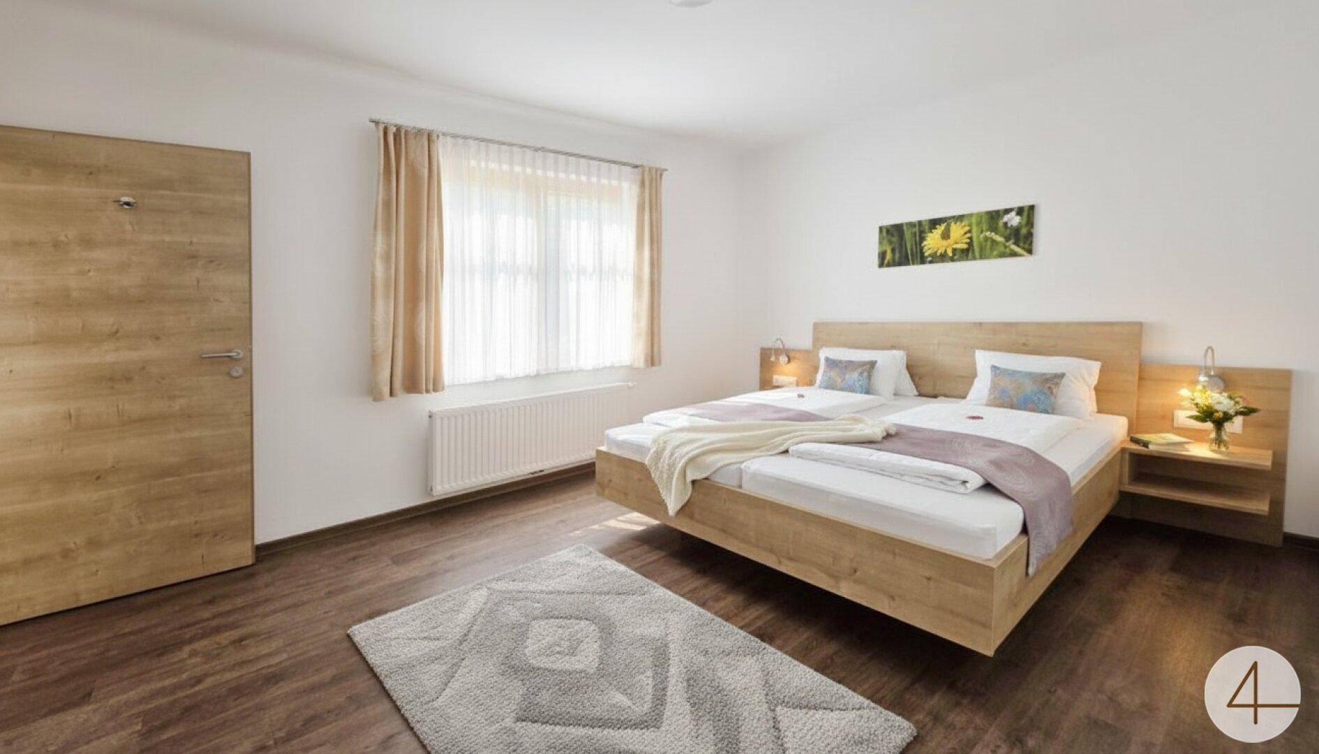 Helles Schlafzimmer mit Doppelbett, Nachttischen und großem Fenster mit Vorhängen.