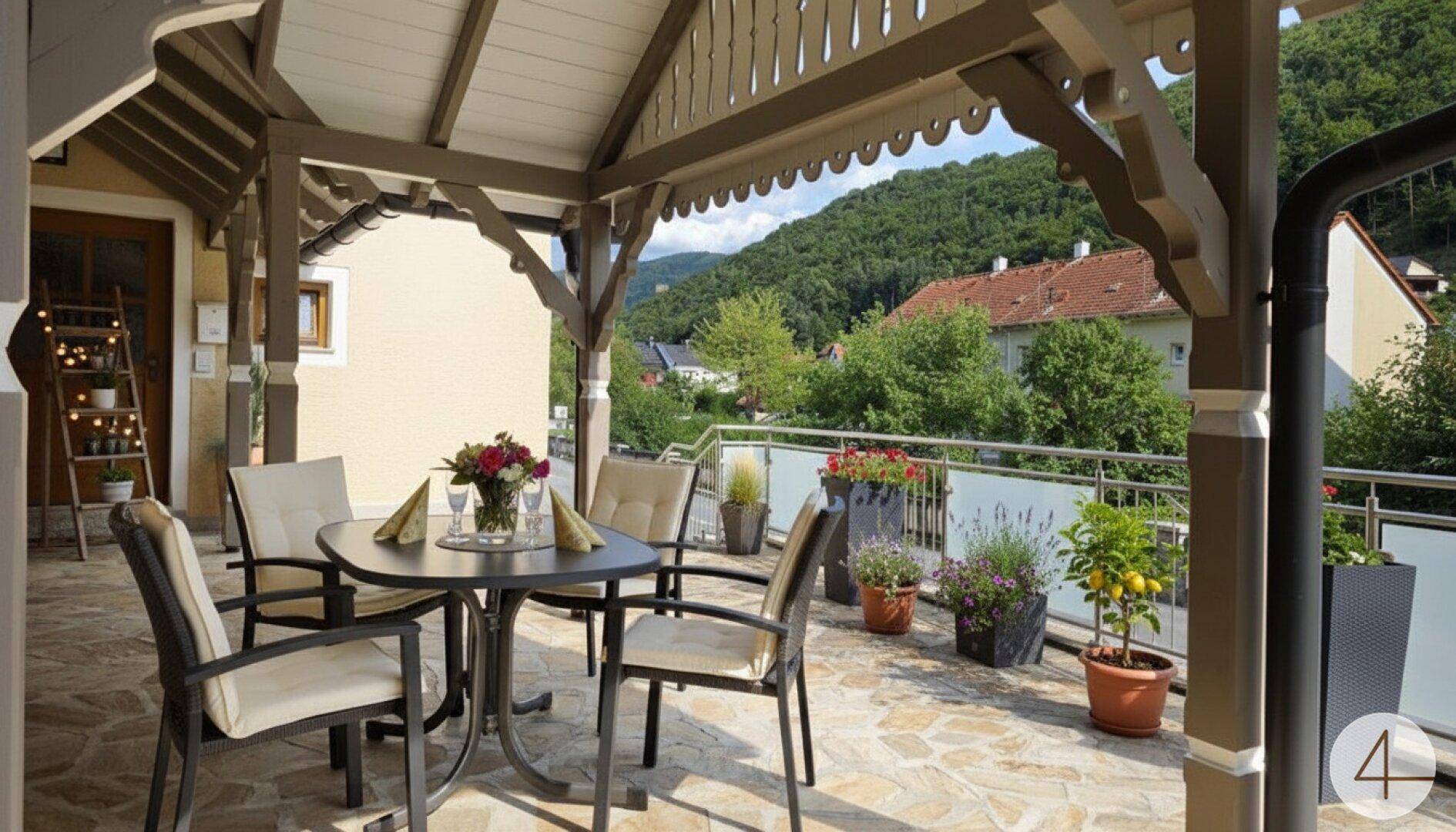 Überdachte Terrasse mit Sitzgelegenheiten, Steinboden und Blick auf die umliegende Landschaft.