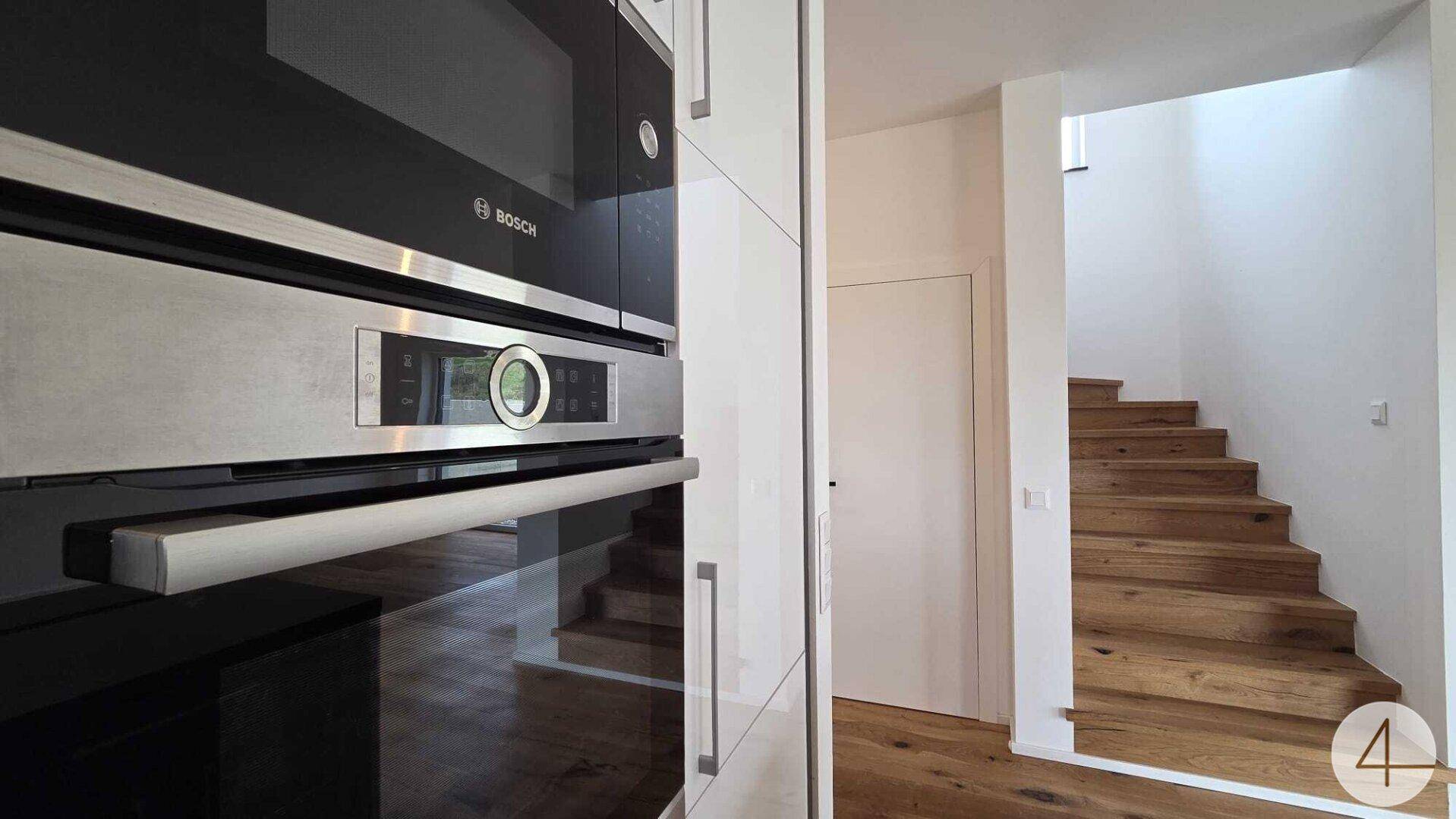 Moderne Einbaugeräte von Bosch in der Küche und eine elegante Holztreppe im Hintergrund.