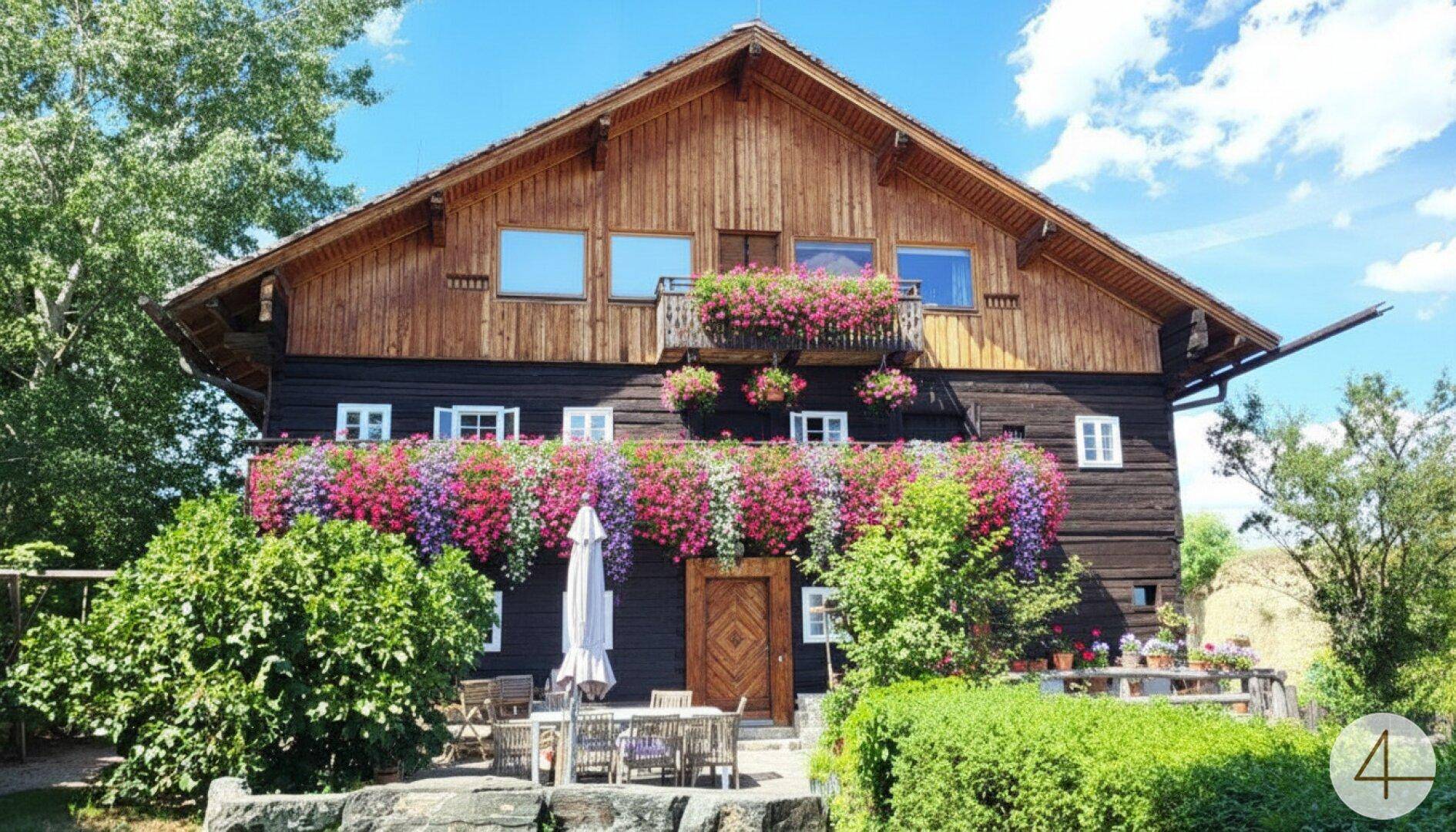 Charmantes Holzhaus mit blühenden Blumenkästen, einer möblierten Terrasse und üppiger Vegetation.