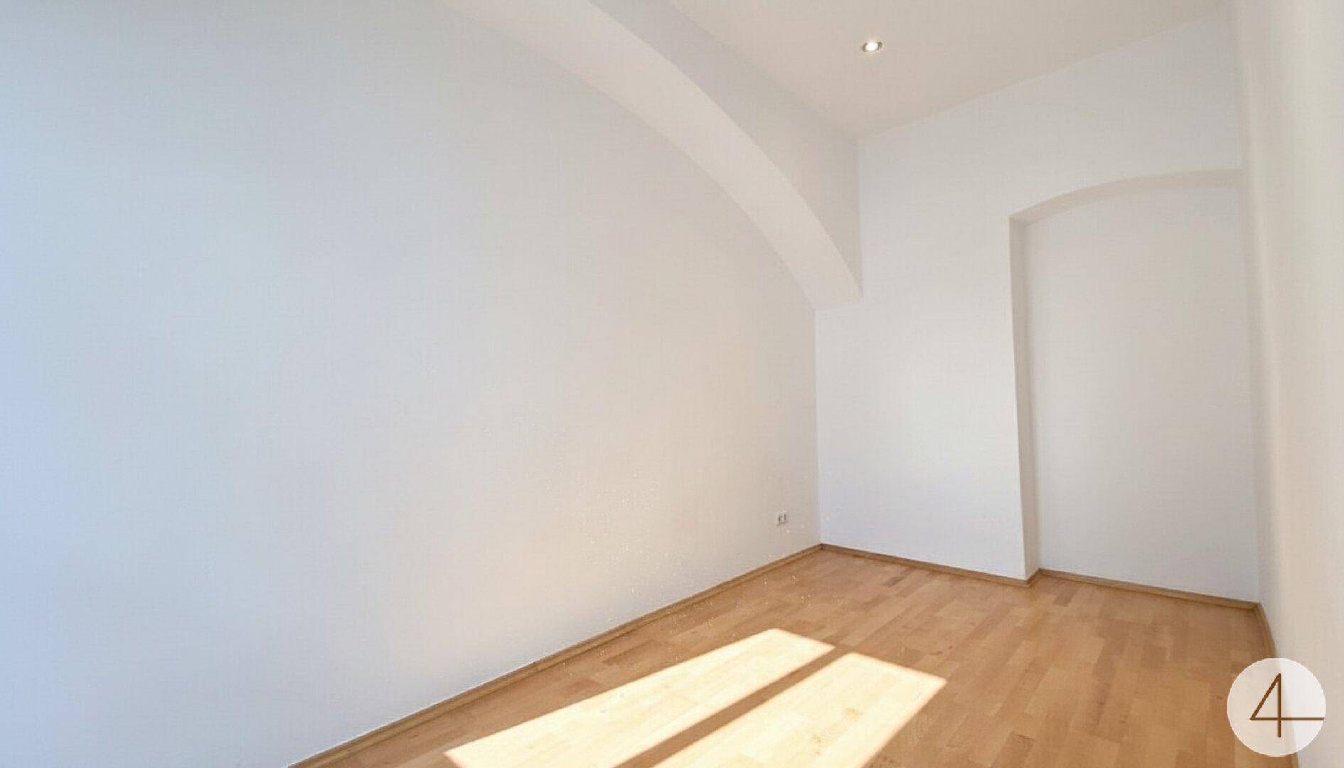 Heller Raum mit Parkettboden, weißen Wänden und einer dekorativen Nische, beleuchtet von Sonnenlicht.