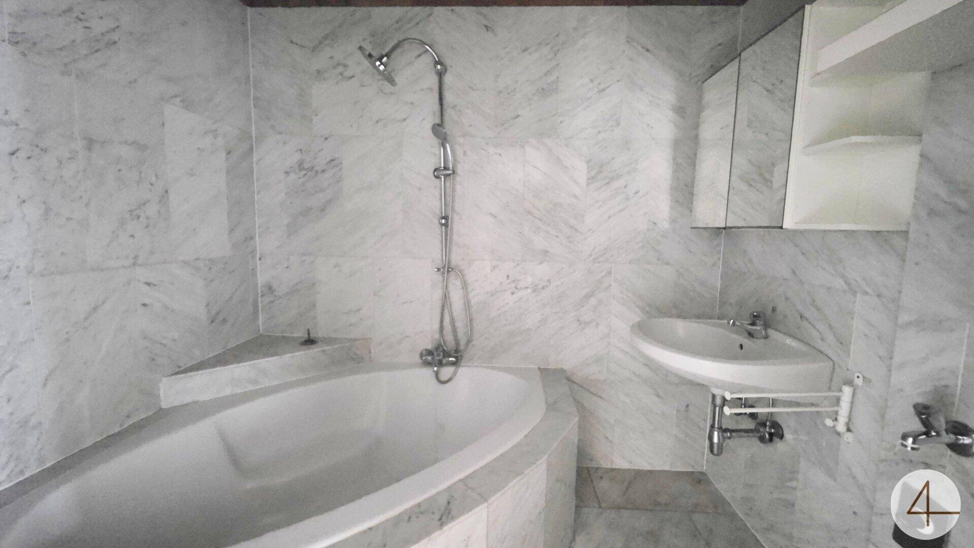 Badezimmer mit Marmorfliesen, einer eingebauten Badewanne und einem Waschbecken mit Spiegelschrank.
