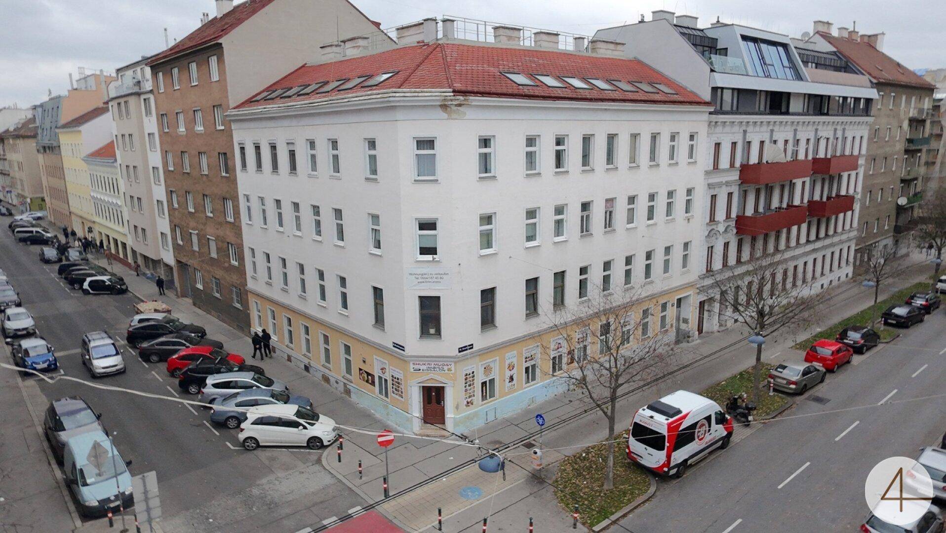 Eckgebäude in städtischer Umgebung mit rotem Dach und parkenden Autos auf der Straße, zeigt die Fassade.