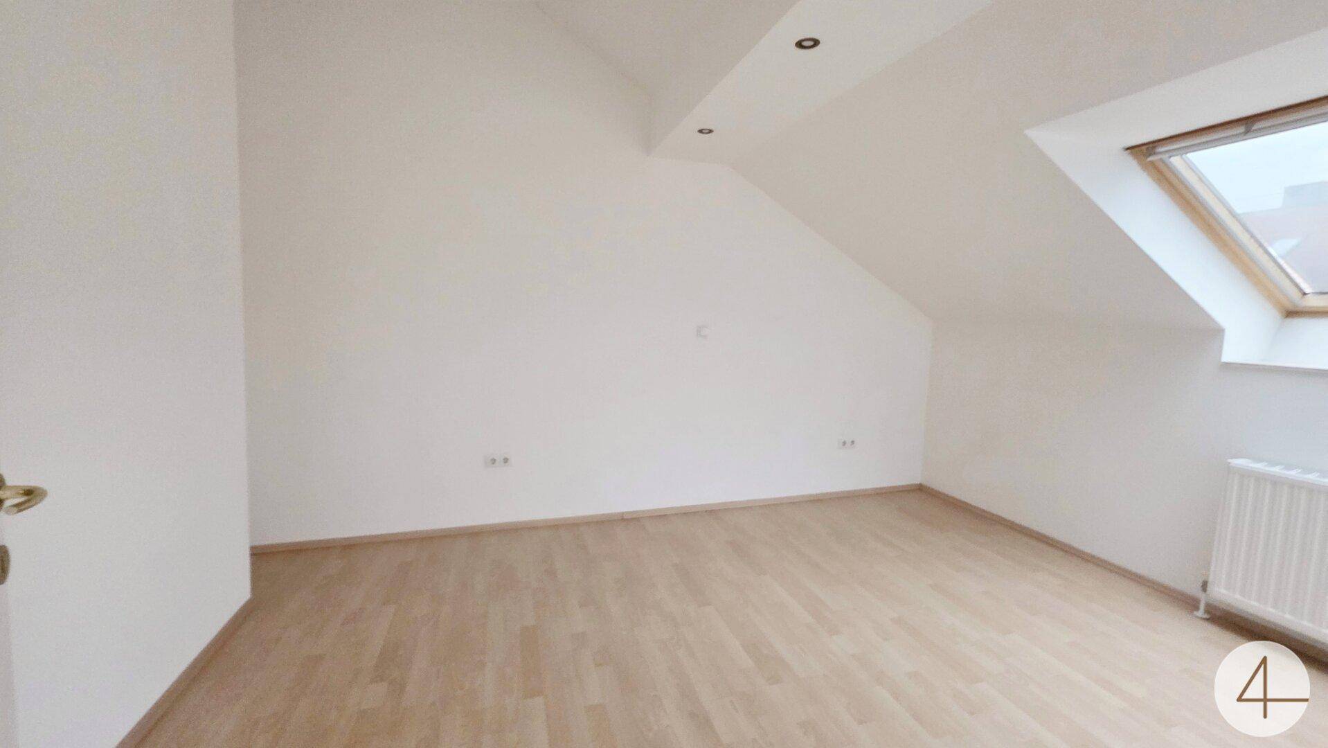 Geräumiges Dachzimmer mit schräger Decke, einem Dachfenster und hellem Laminatboden.