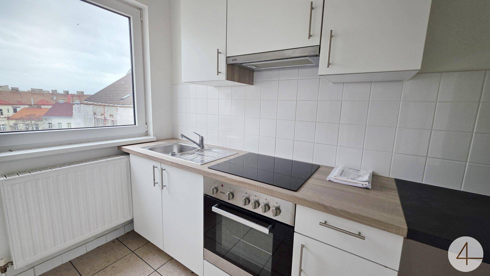 Funktionale Küche mit weißen Schränken, Induktionskochfeld und Fensterblick.