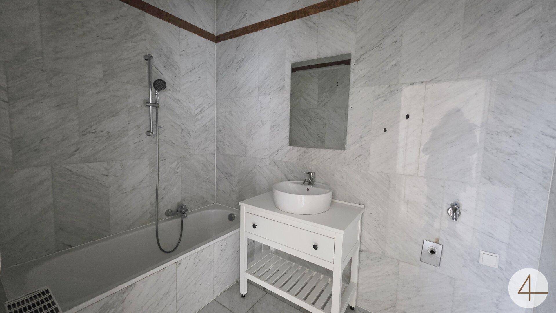 Modernes Badezimmer mit Marmorfliesen, Badewanne und Aufsatzwaschbecken.