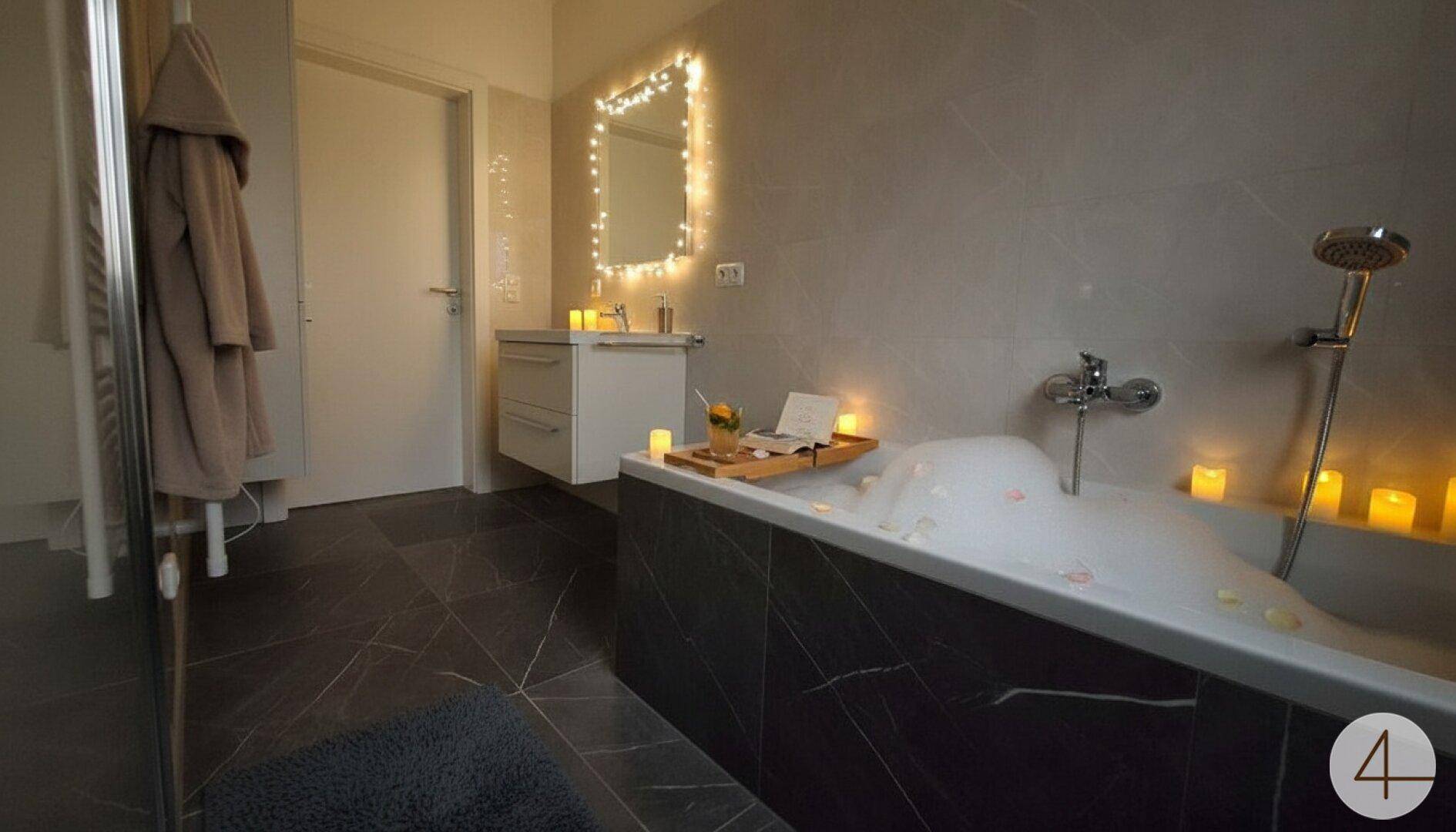 Entspannendes Badezimmer mit Badewanne, stimmungsvoller Beleuchtung und dunklen Fliesen.
