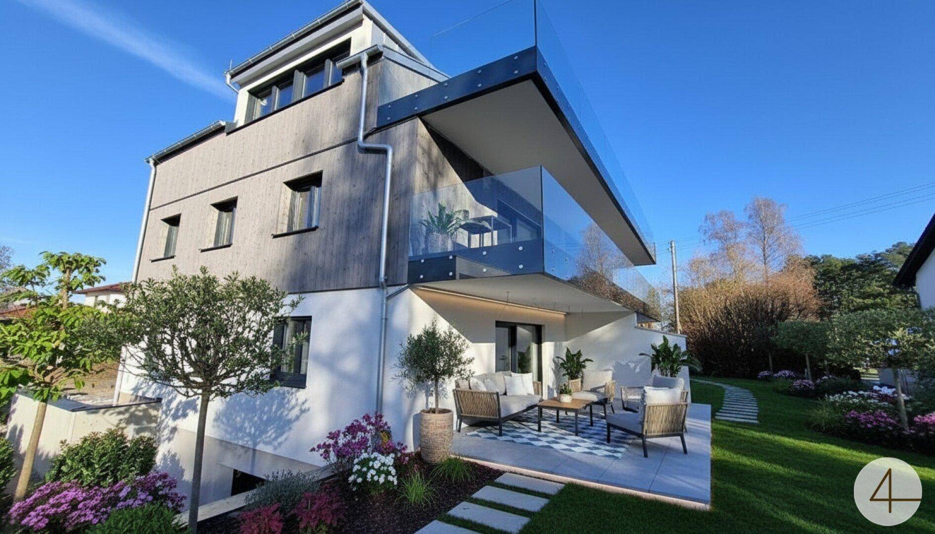 Modernes Gebäude mit großer Terrasse, Glasgeländer und gepflegtem Gartenbereich.