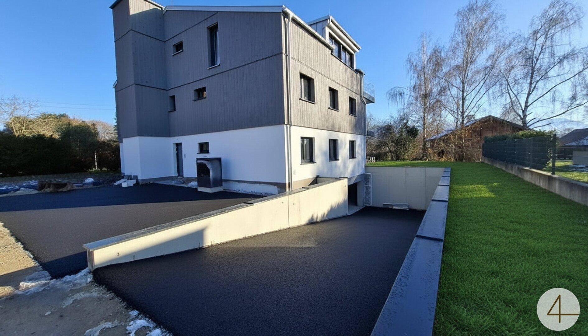Modernes Gebäude mit Zufahrt zur Tiefgarage und gepflegter Rasenfläche.
