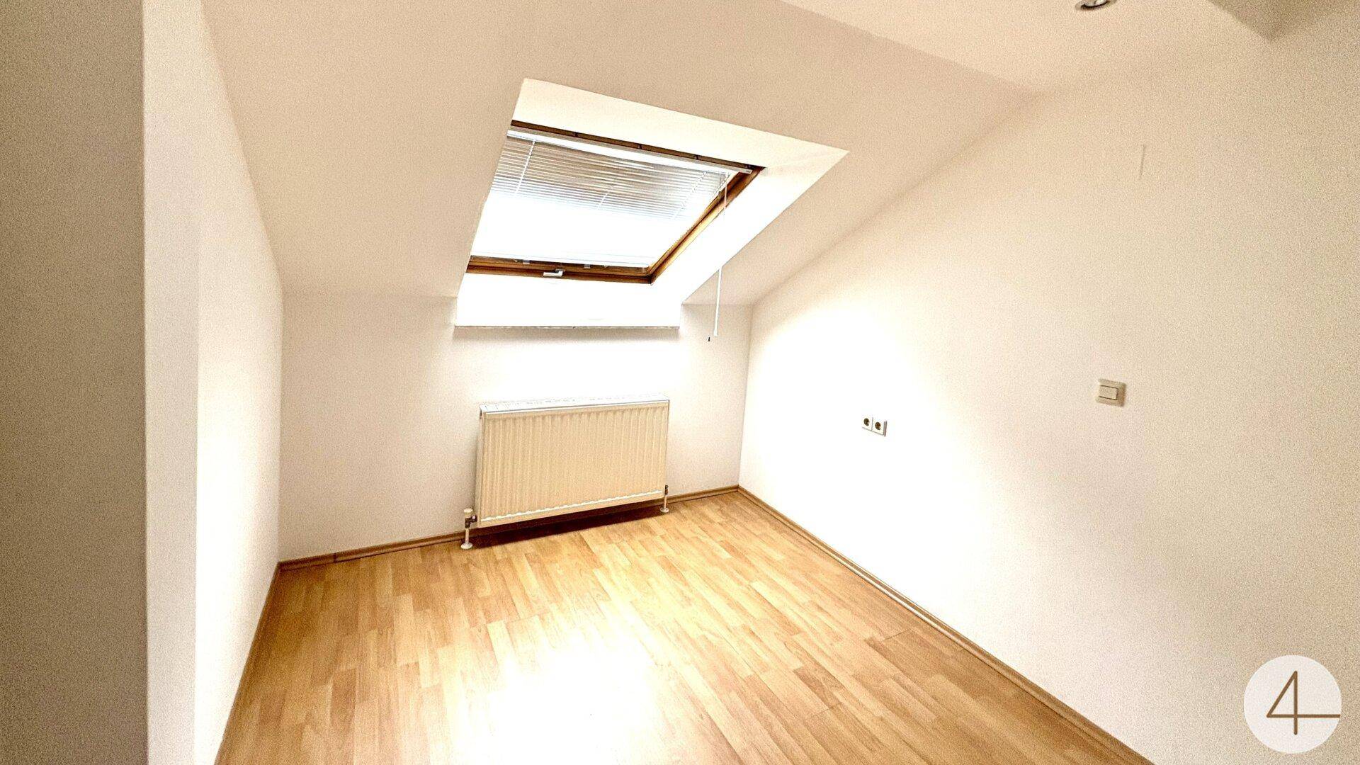 Kleineres Zimmer im Dachgeschoss mit einem Dachfenster und hellem Holzboden.