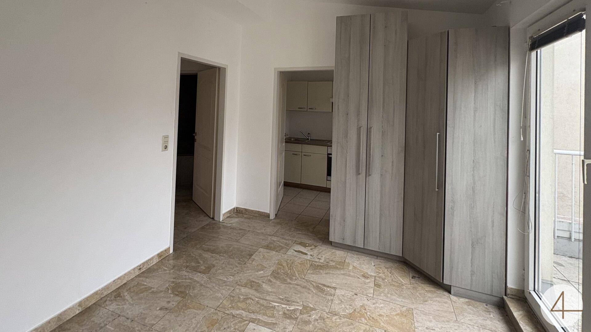 Zimmer mit Fliesenboden, Einbauschrank und Zugang zu einer kleinen Küchenzeile.