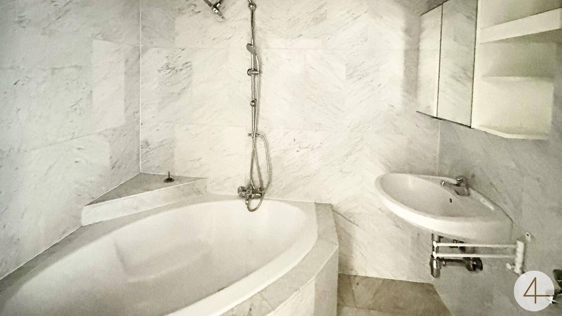 Badezimmer mit Marmorfliesen, Badewanne und Waschbecken, ausgestattet mit Spiegelschrank.