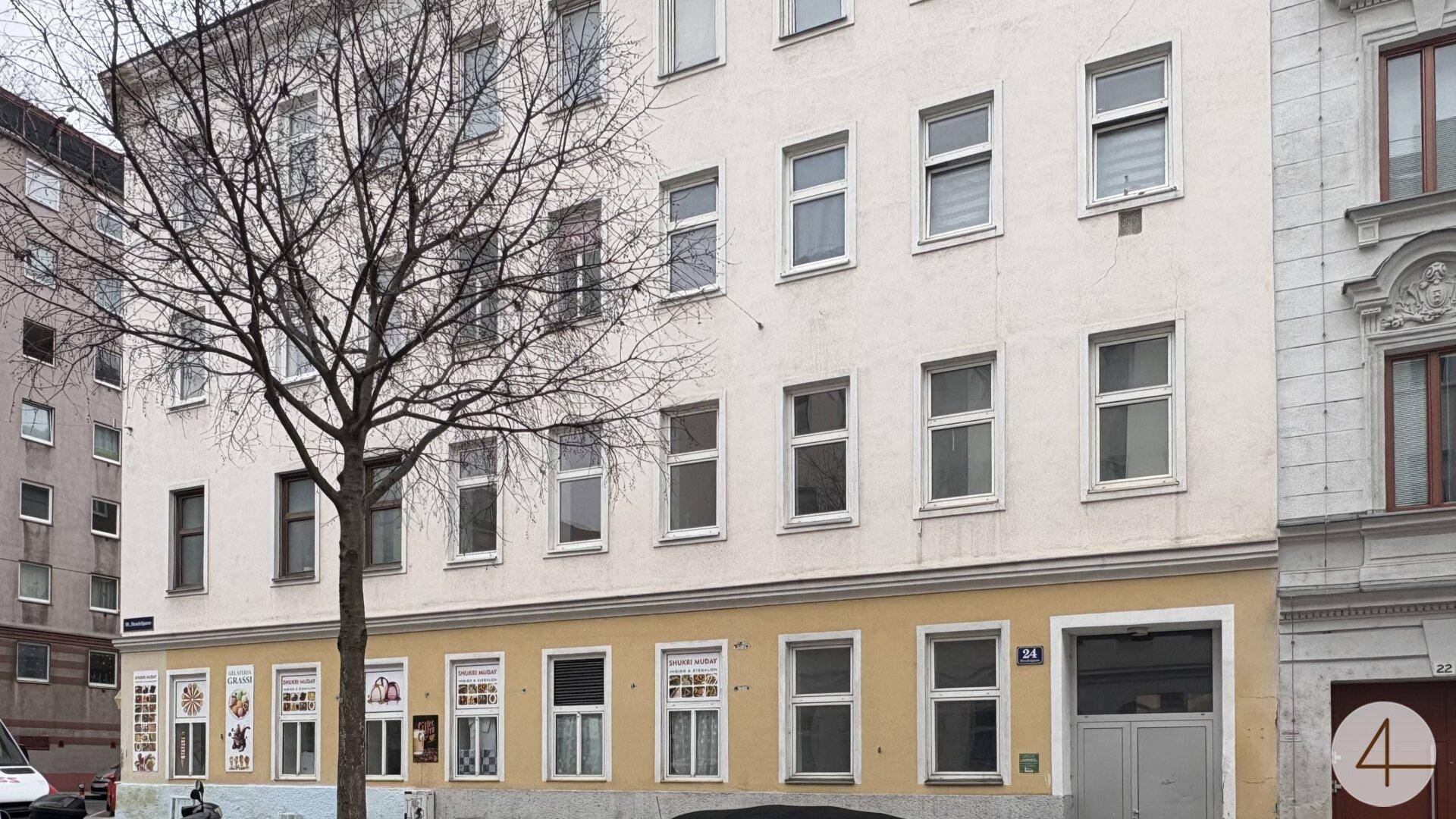 Fassade eines Mehrfamilienhauses mit vielen Fenstern und einem Baum im Vordergrund.